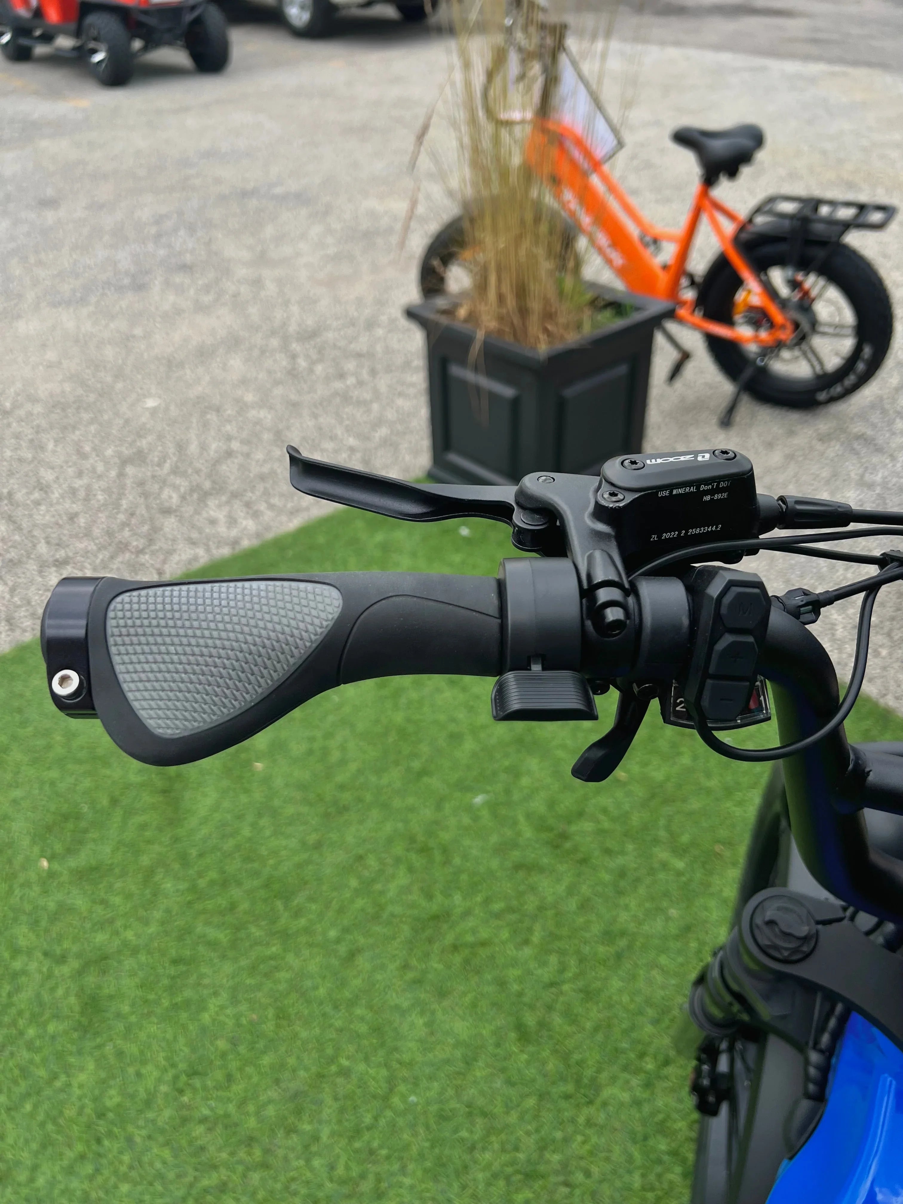Electric bike handlebar with ergonomic grip and controls, orange ebike in background