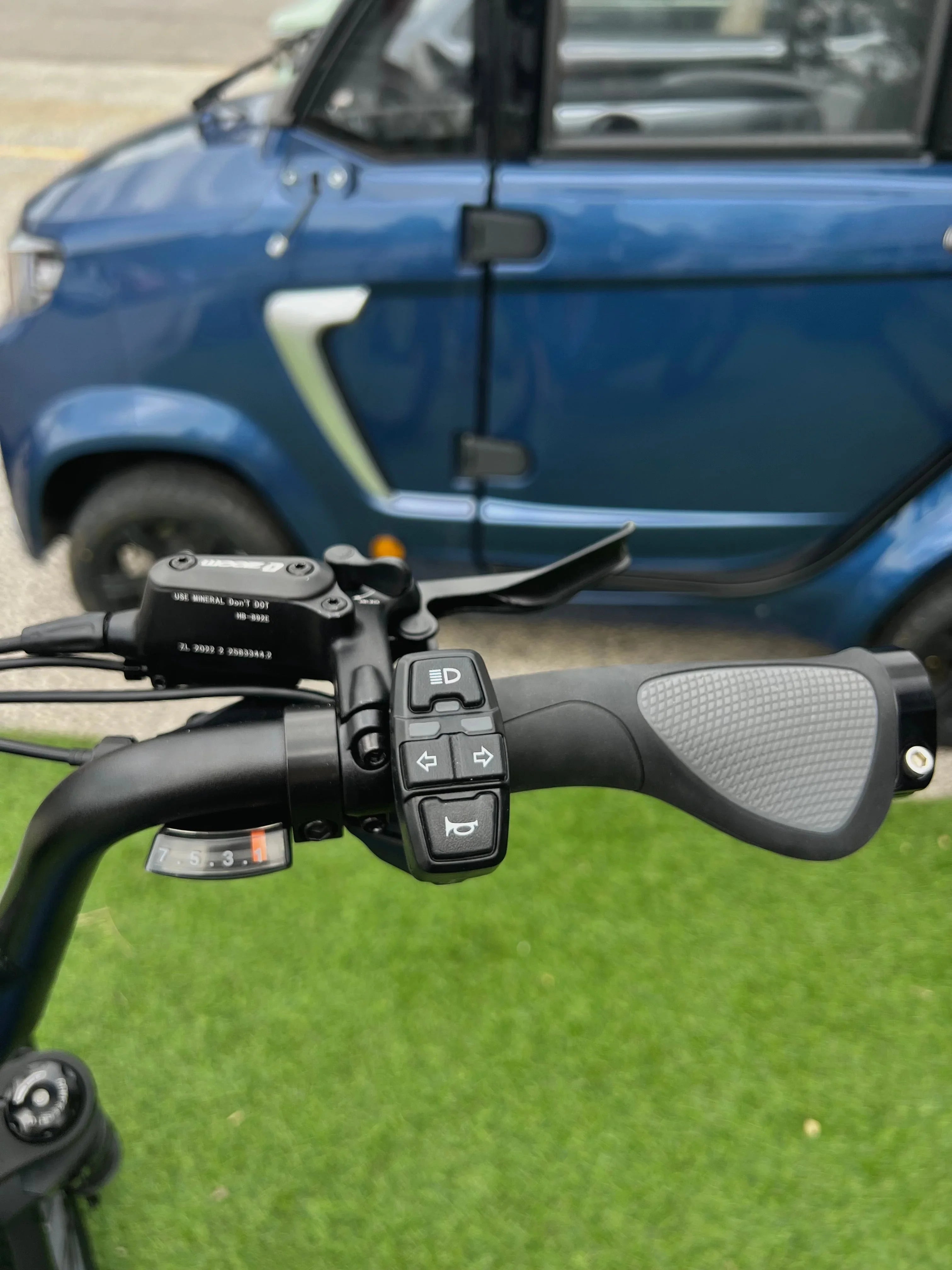 Electric bike handlebar with control buttons, parked near a blue compact electric car