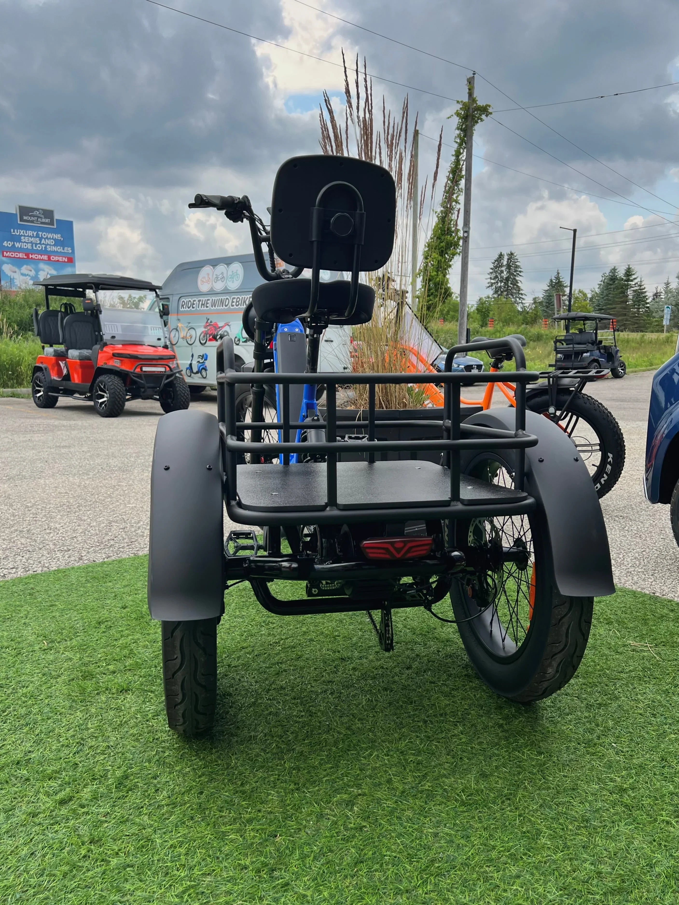 Rear view of electric tricycle on grass, outdoor dealership, golf carts in background