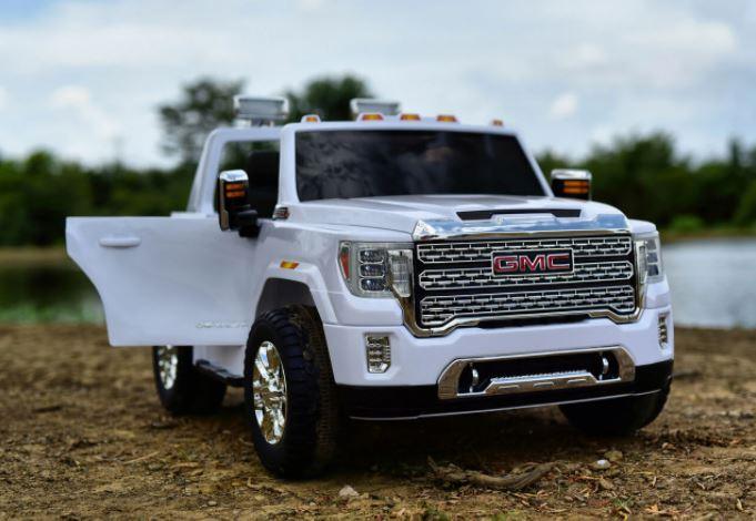 White GMC toy truck with open door outdoors on dirt by water and trees