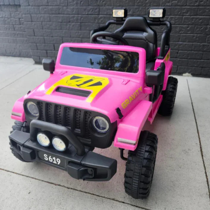 Pink toy Jeep ride-on car with yellow accents and 'GRAVITY' text, parked on pavement