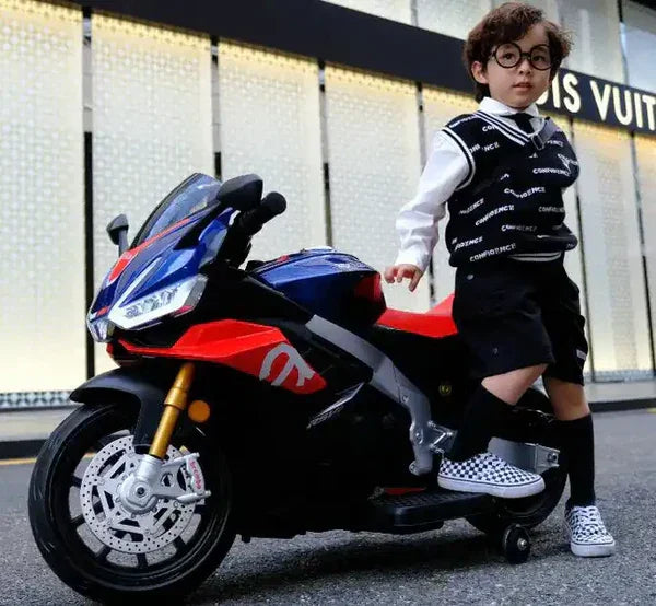 Child posing with blue and red 12V Aprilia toy motorcycle on city street
