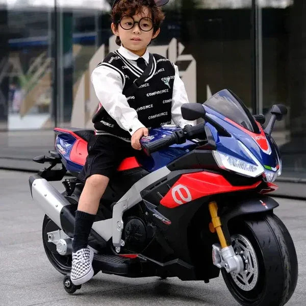 Child on blue and red 12V Aprilia toy motorcycle outside, wearing glasses and black vest