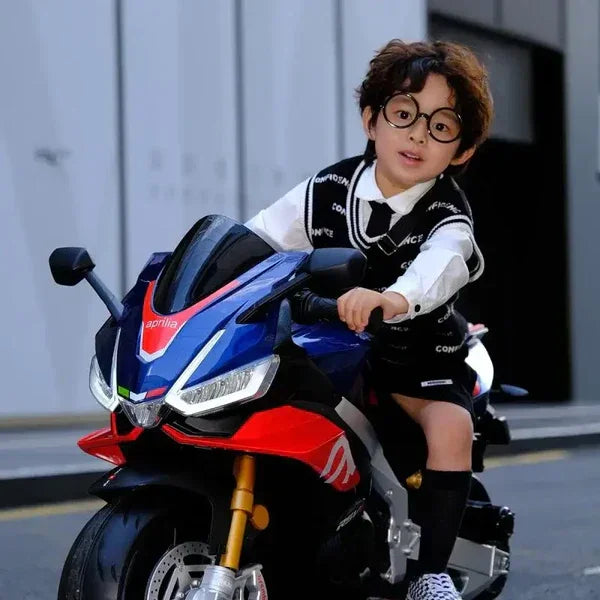 Child riding blue Aprilia toy motorcycle outdoors, wearing glasses and school uniform.