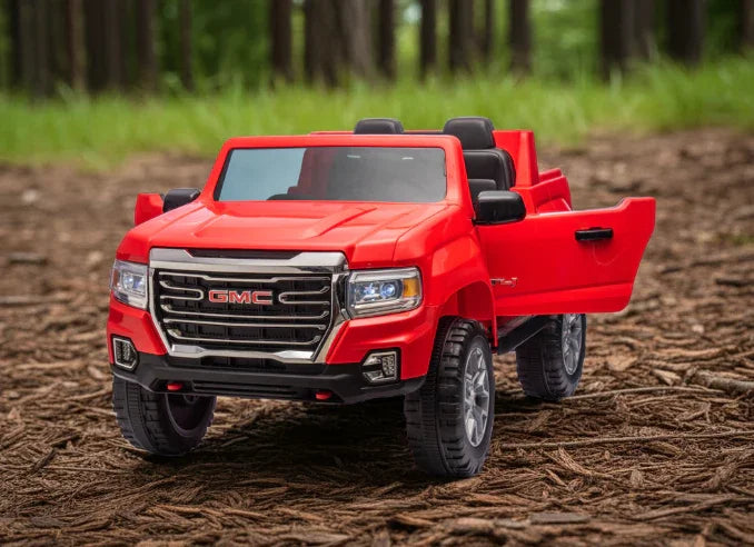 Red GMC toy truck with open door parked outdoors on wood chips, forest background