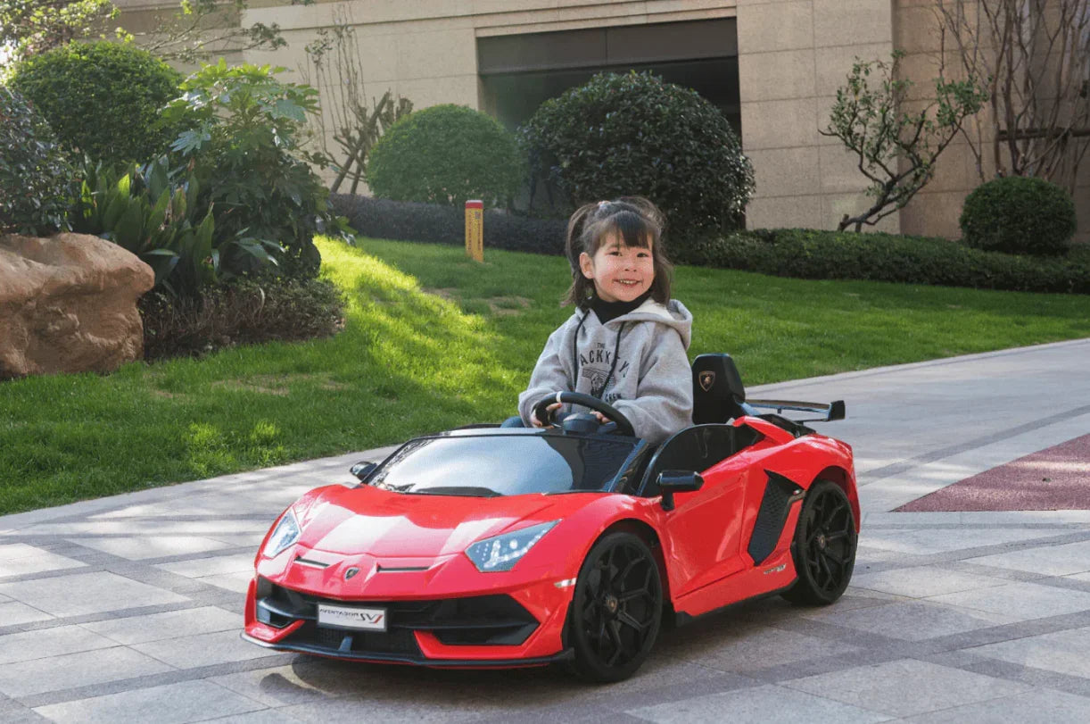 Smiling child driving red Lamborghini Aventador SV kids ride-on car outdoors