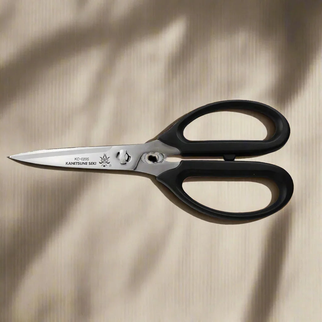 Kanetsune Seki stainless steel scissors with black handles on a beige surface
