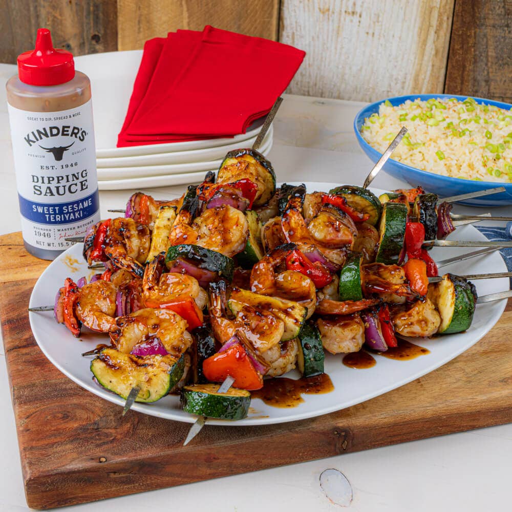 Grilled shrimp and vegetable skewers glazed with teriyaki sauce, served with rice on a plate.