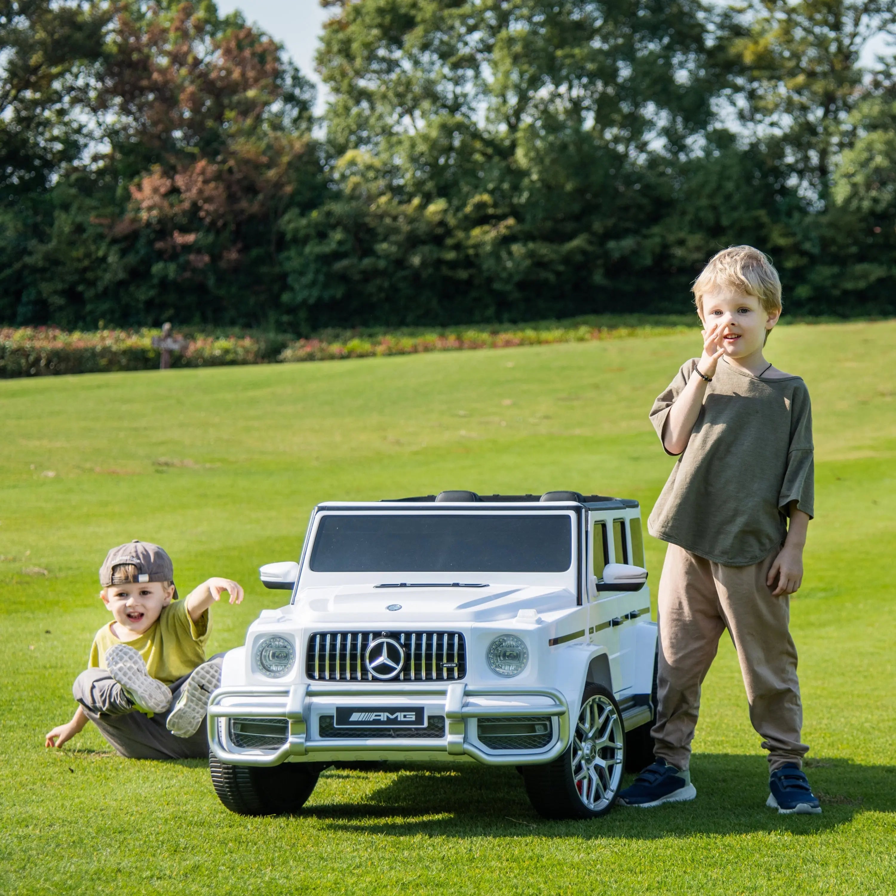 Kids playing outdoors with a white Mercedes G63 AMG 4x4 ride-on car on grass