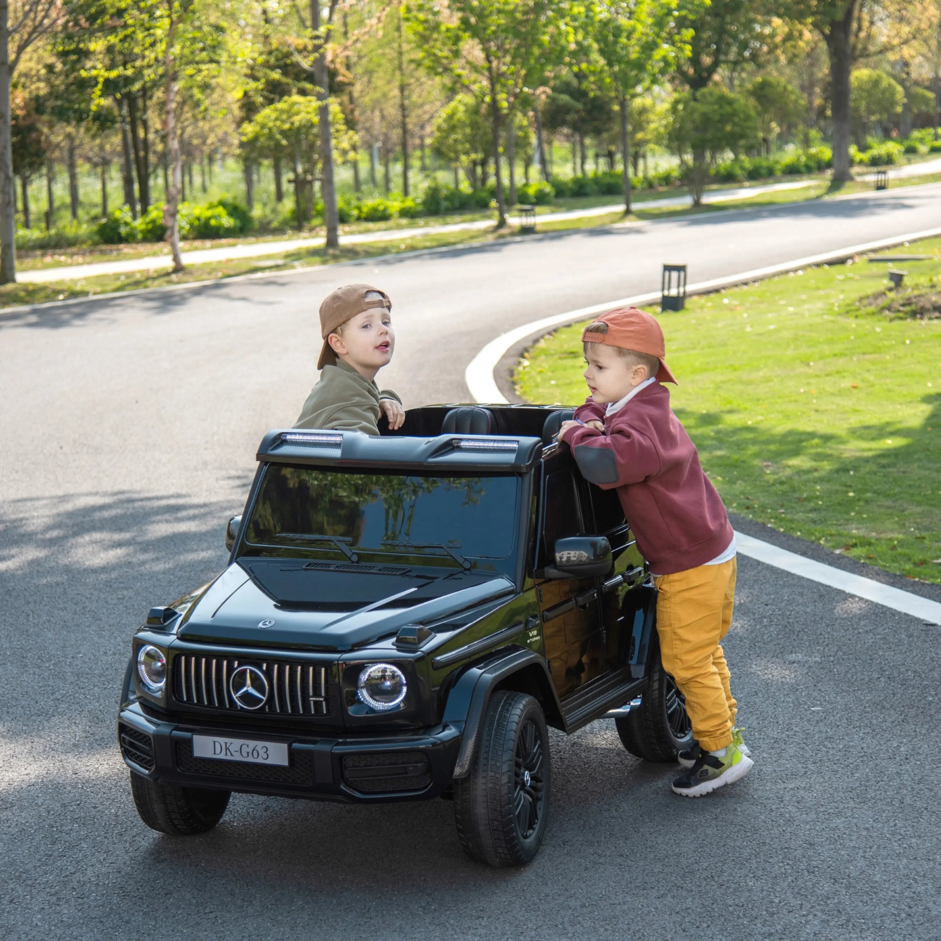 Two kids playing with a black ride-on Mercedes-Benz G-Wagon toy car outdoors