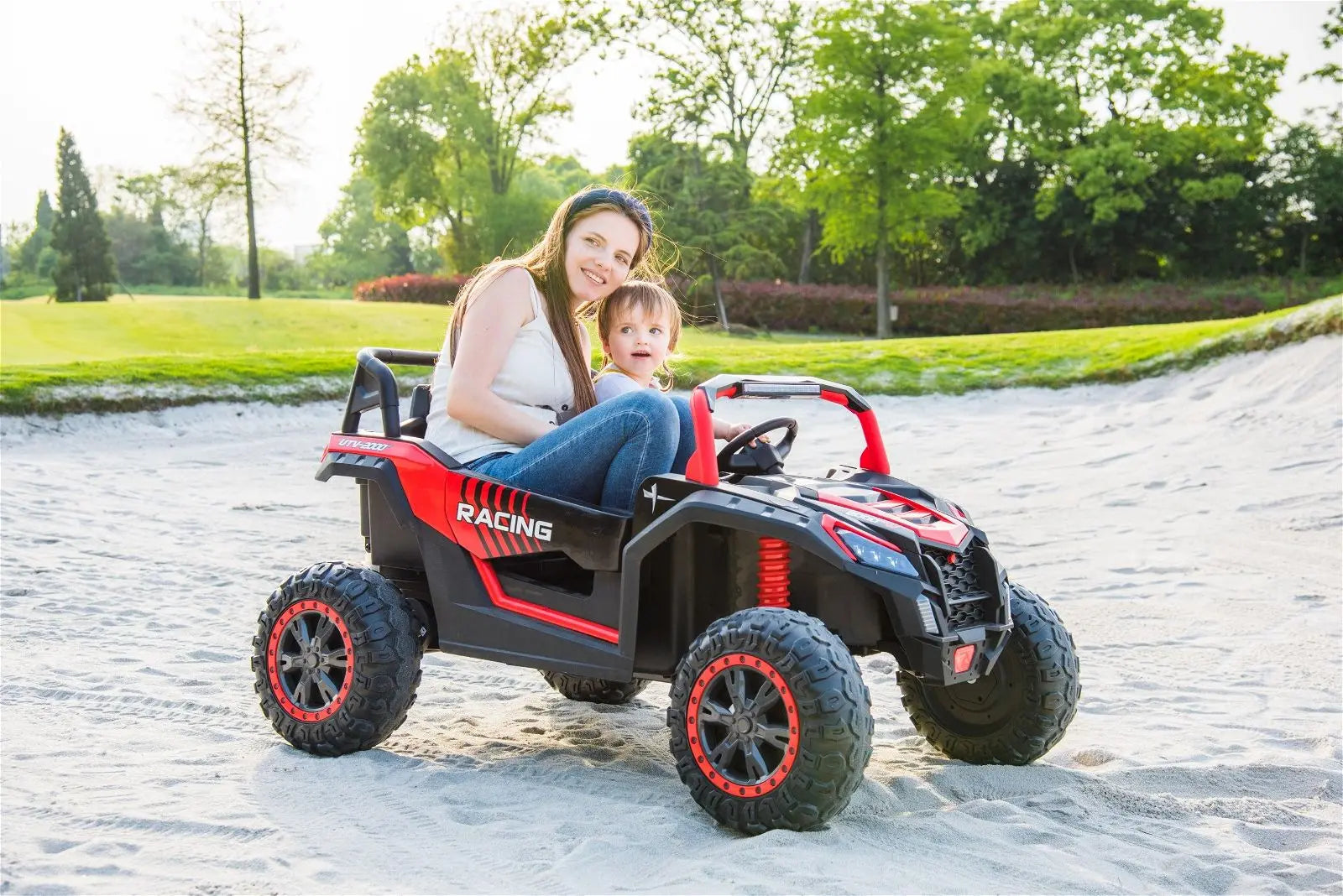 Woman and child riding a red 2-seater kids dune buggy toy outdoors on sand