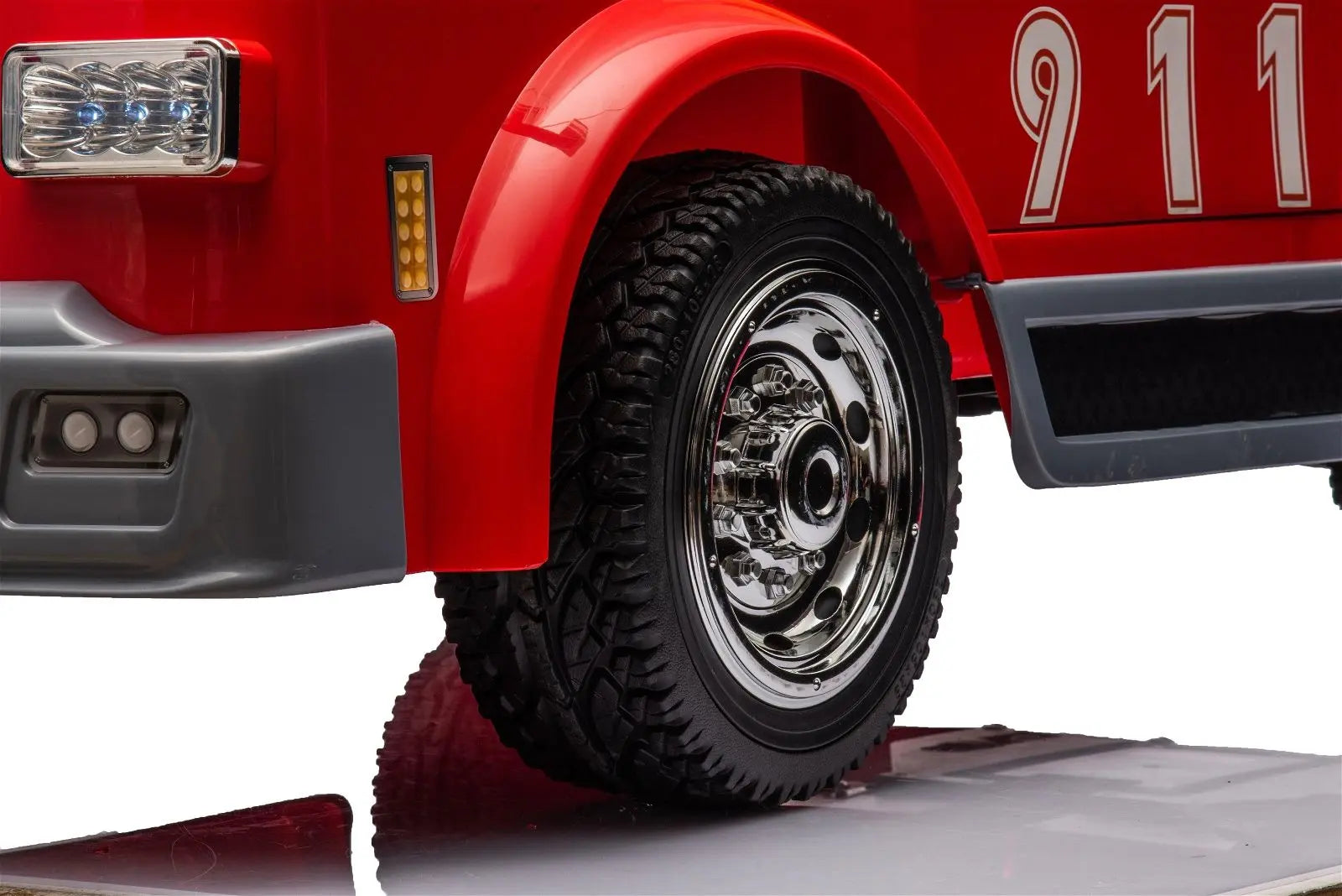 Close-up of red 24V ride-on fire truck wheel, chrome rim, treaded tire, and 911 decals