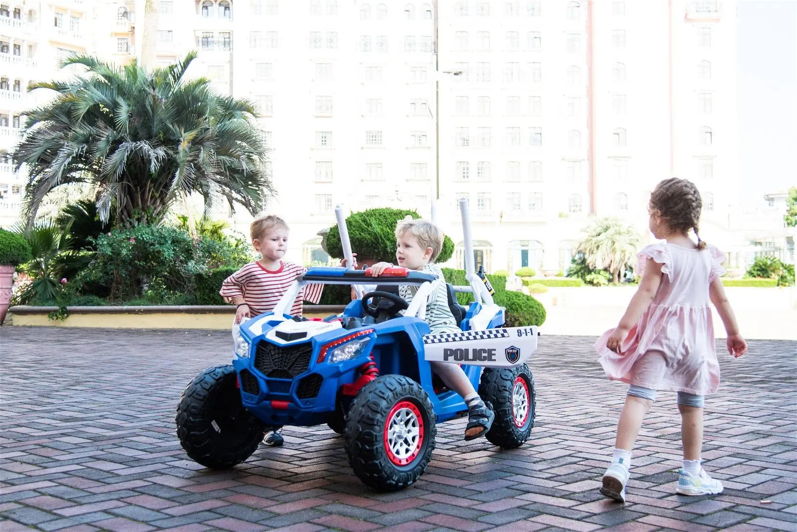 Kids playing outdoors with a blue ride-on police UTV toy featuring lights and sirens
