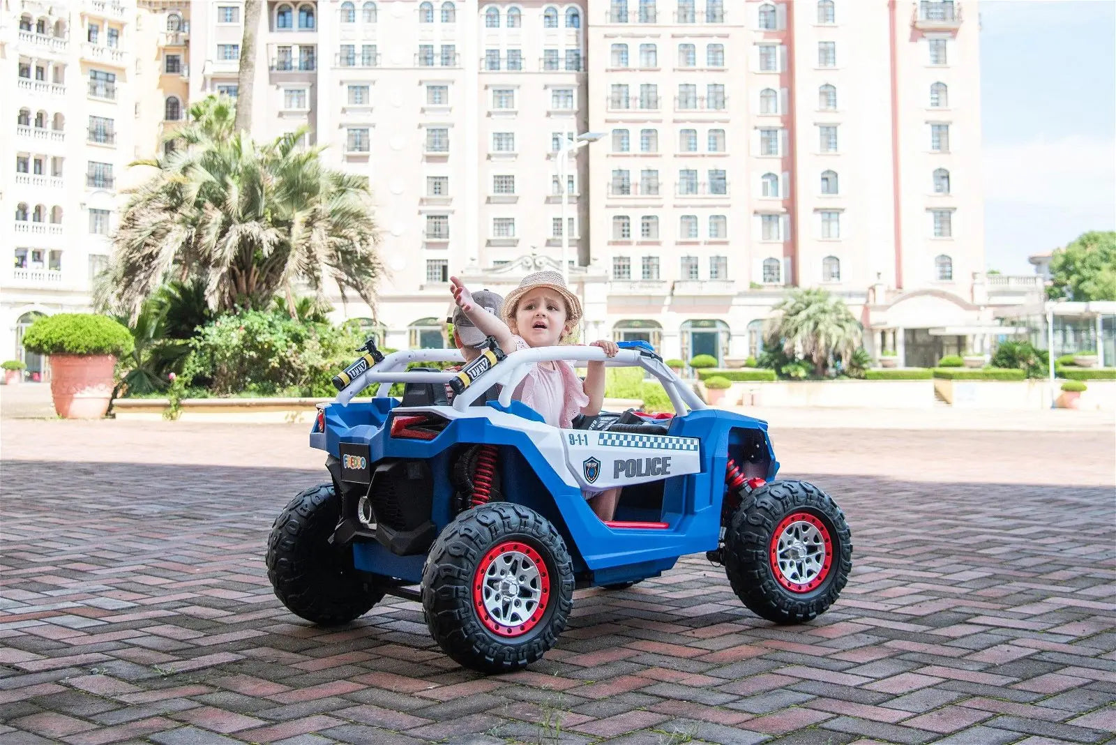 Child riding blue 2-seater electric police UTV toy car outdoors in a city courtyard