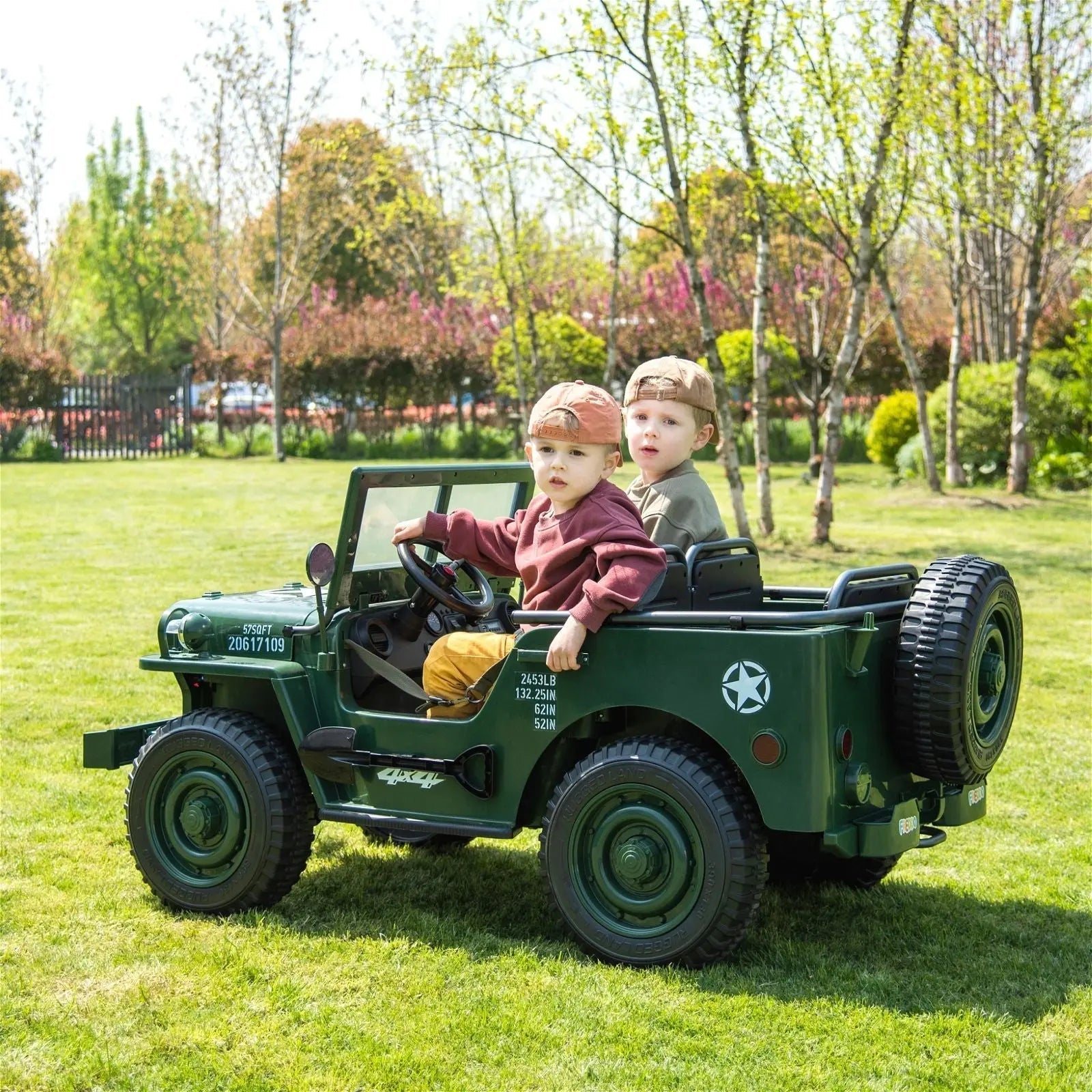 Two kids riding a green 24V military-style electric Jeep toy outdoors on grass