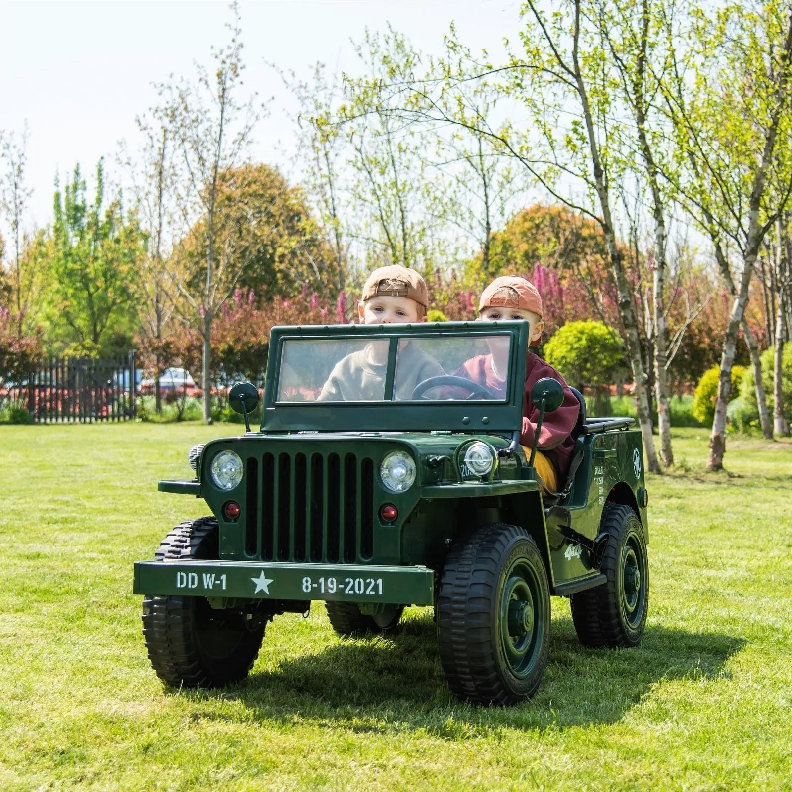 Children driving a green 3-seater electric ride-on jeep outdoors on grass