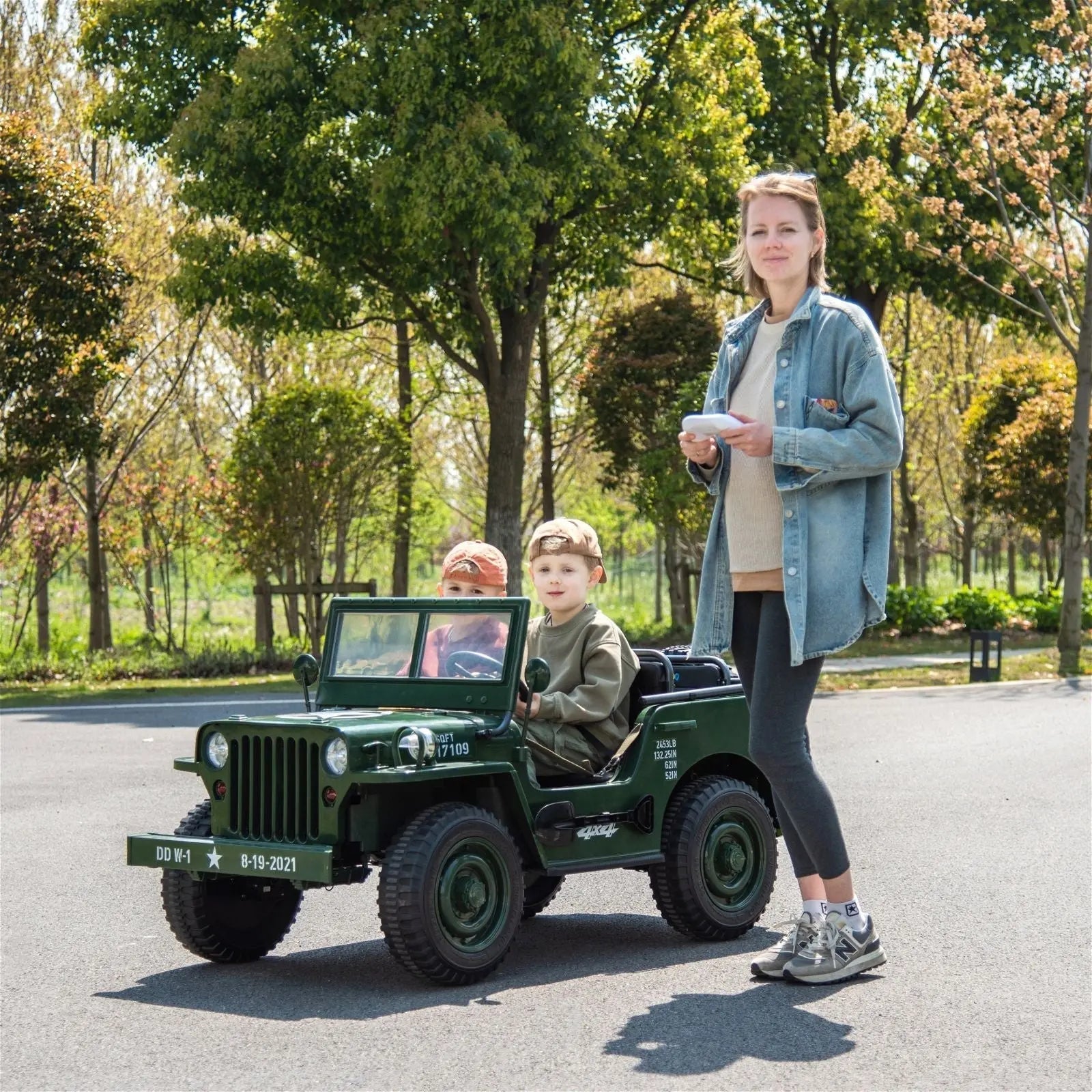 Kids riding green electric military-style jeep outdoors with adult supervising