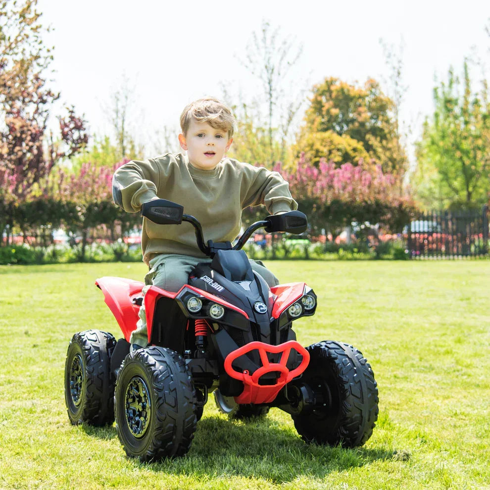 Young boy riding red kids electric ATV quad bike outdoors on green grass
