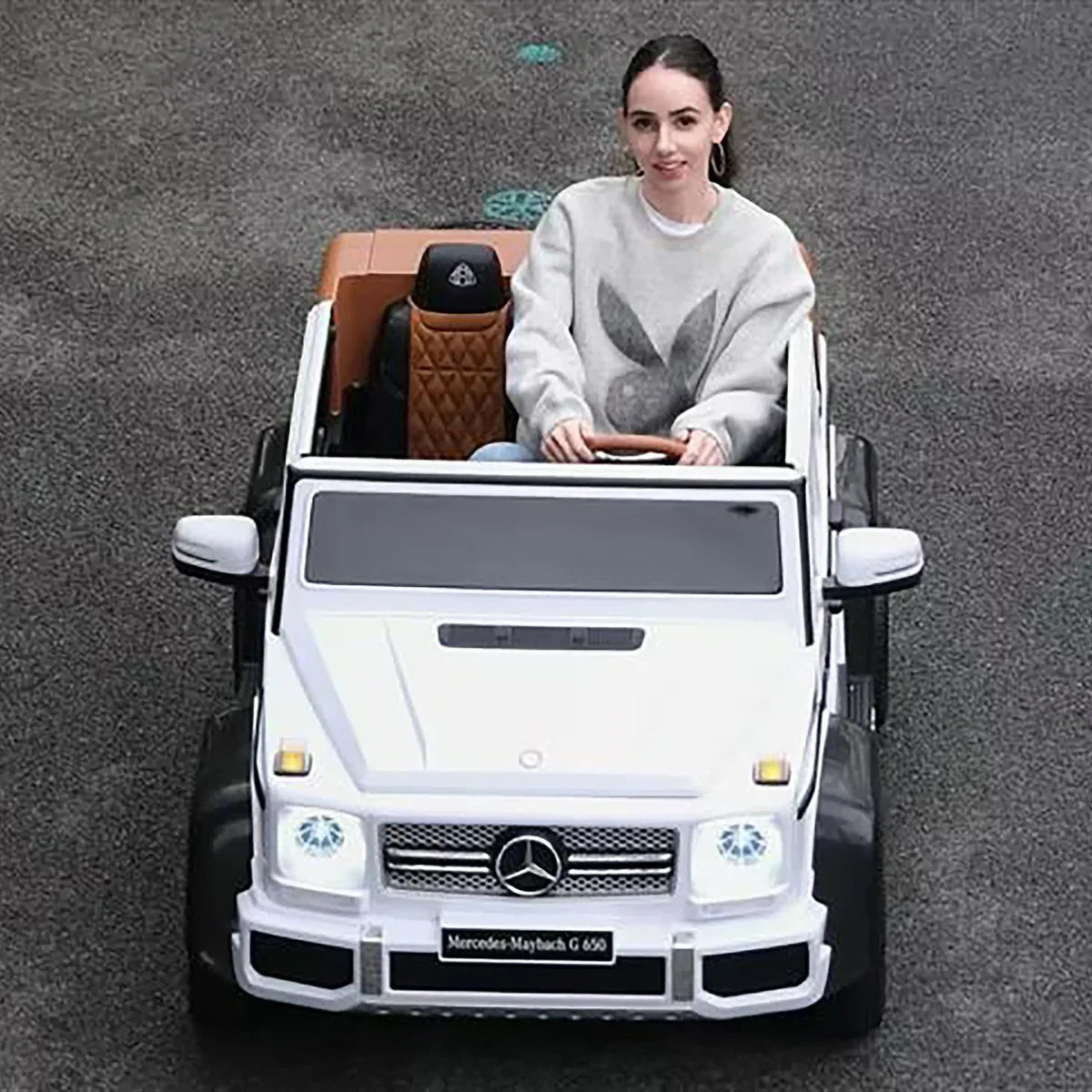 Woman driving white Mercedes-Maybach G 650 toy car on asphalt, luxury ride-on vehicle