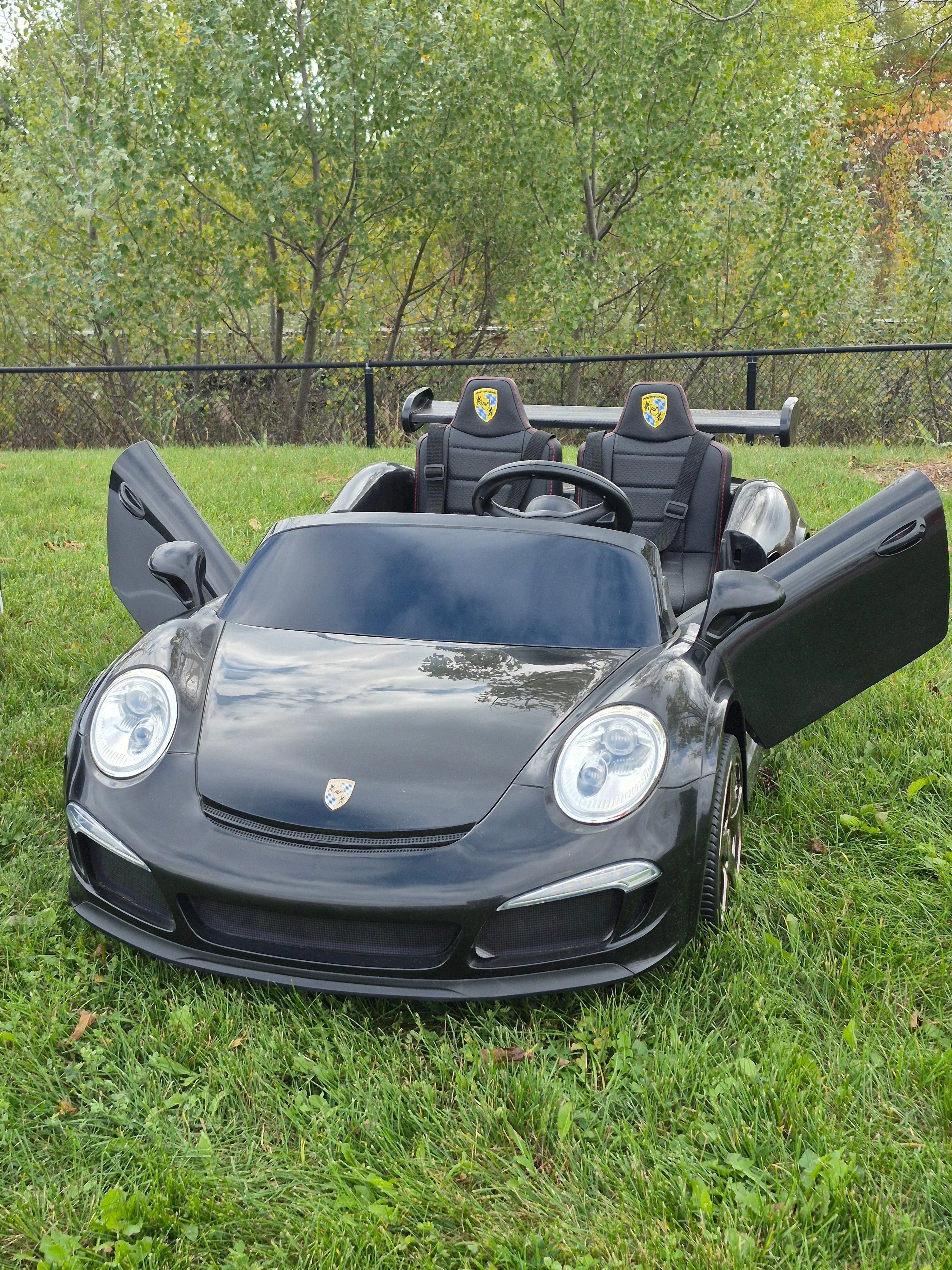 Black kids electric ride-on sports car with open doors on grass in outdoor setting