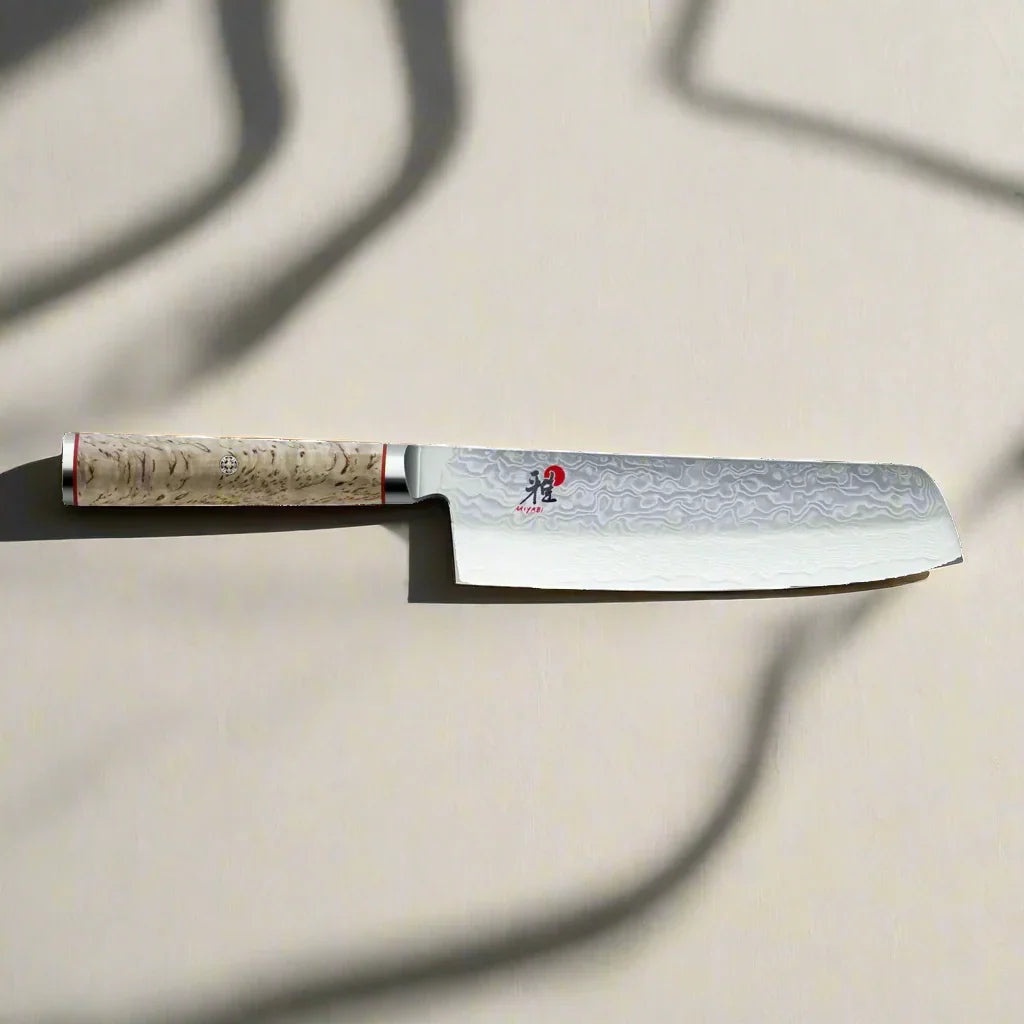 Japanese Damascus steel nakiri knife with light wood handle on a cream background