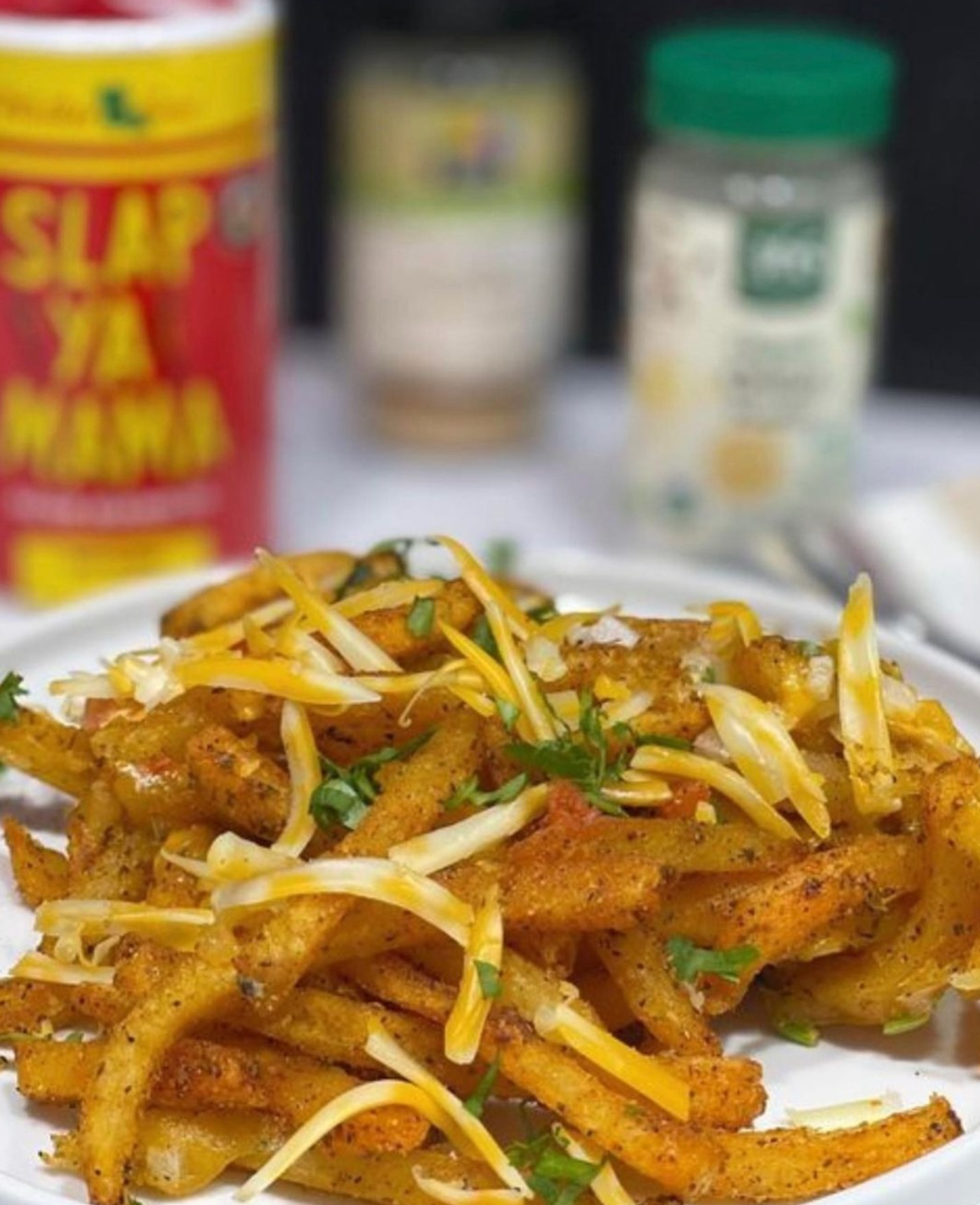 Seasoned French fries with shredded cheese and fresh herbs on a white plate