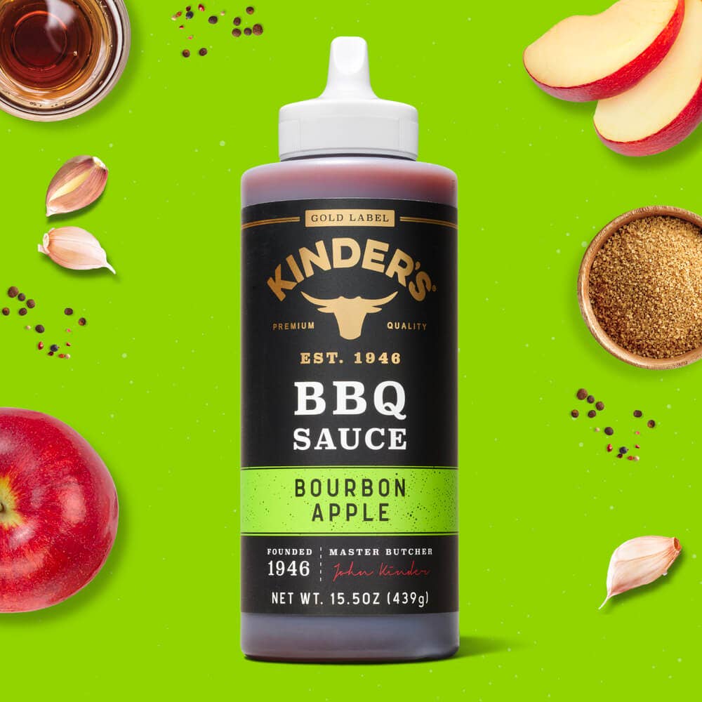 Kinder's Bourbon Apple BBQ sauce bottle with apples, garlic, brown sugar and spices on green background