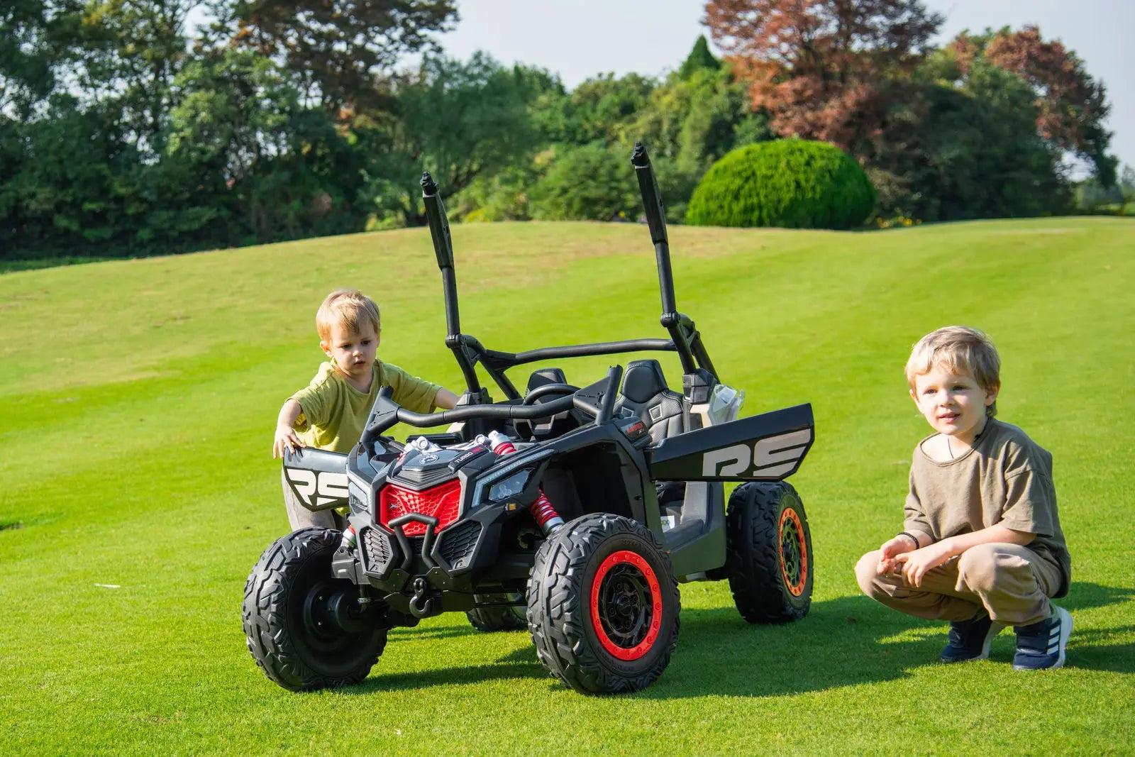 Two children with a black 2-seater ride-on UTV for kids on grass outdoors
