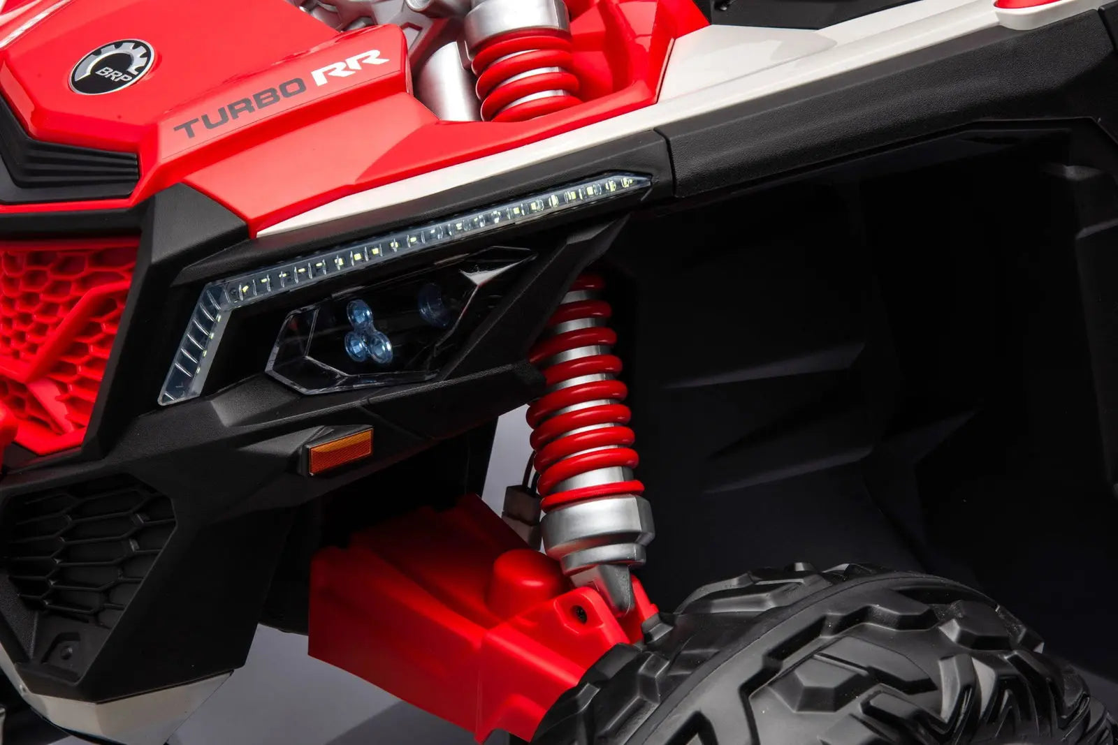 Red Can-Am Maverick kids ride-on UTV close-up showing LED headlight, shock absorber, rugged tire