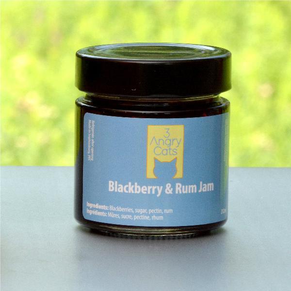 Jar of 3 Angry Cats Blackberry & Rum Jam on outdoor table with green blurred background