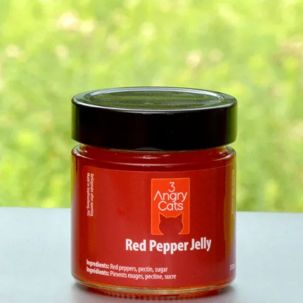 Jar of 3 Angry Cats red pepper jelly on outdoor table with green blurred background