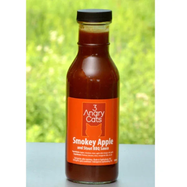 Bottle of 3 Angry Cats Smokey Apple Stout BBQ sauce outdoors with green background