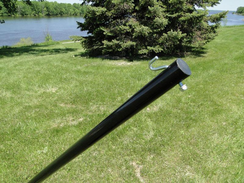 Black steel hammock stand arm in grassy outdoor setting near a lake and pine trees
