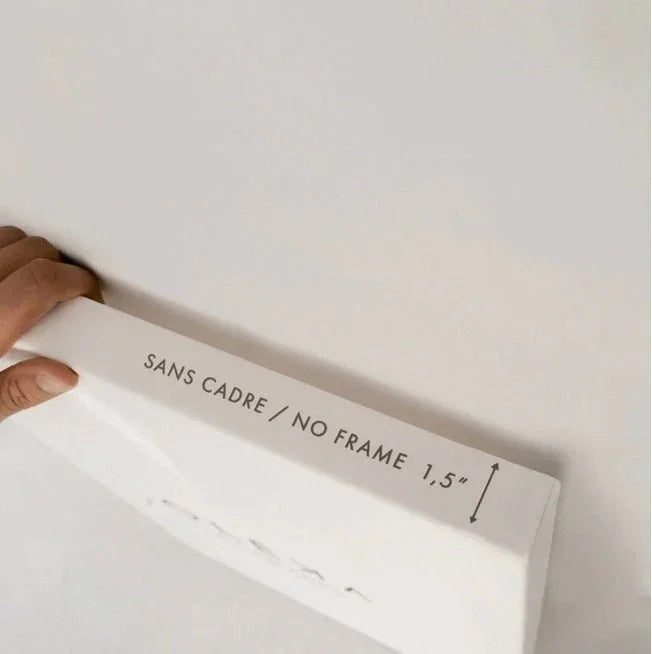 Hand holding canvas edge labeled 'No Frame 1.5 inch', close-up against white wall.