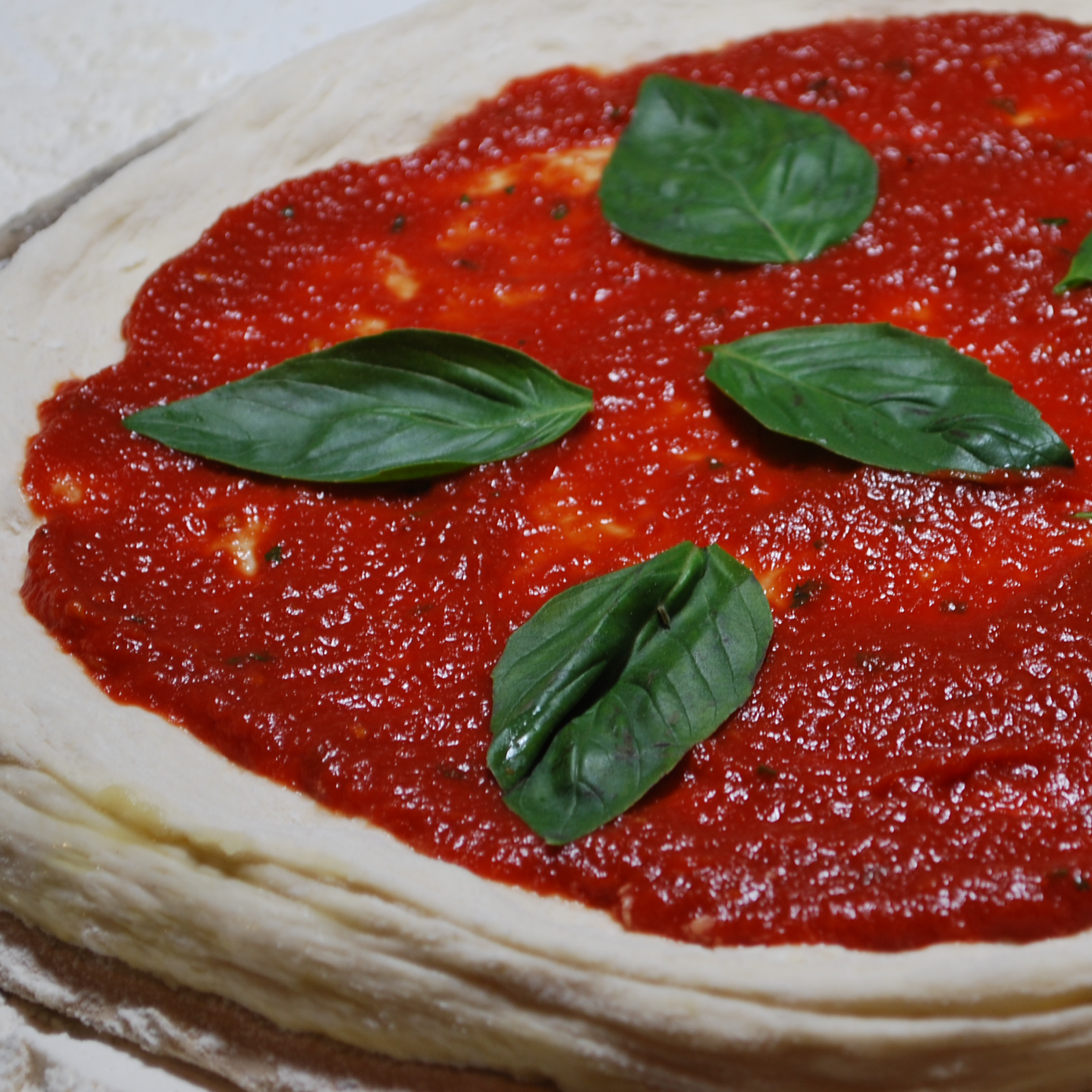 Unbaked pizza dough with tomato sauce and fresh basil leaves