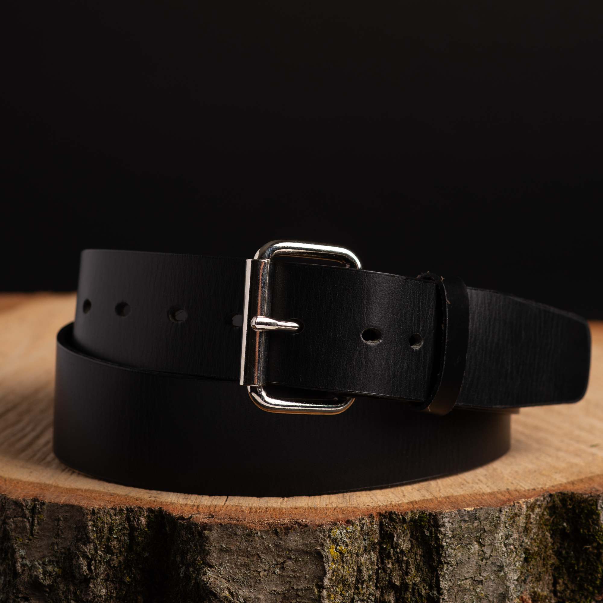 Black leather belt with silver buckle on wooden log, outdoor camping gear accessory