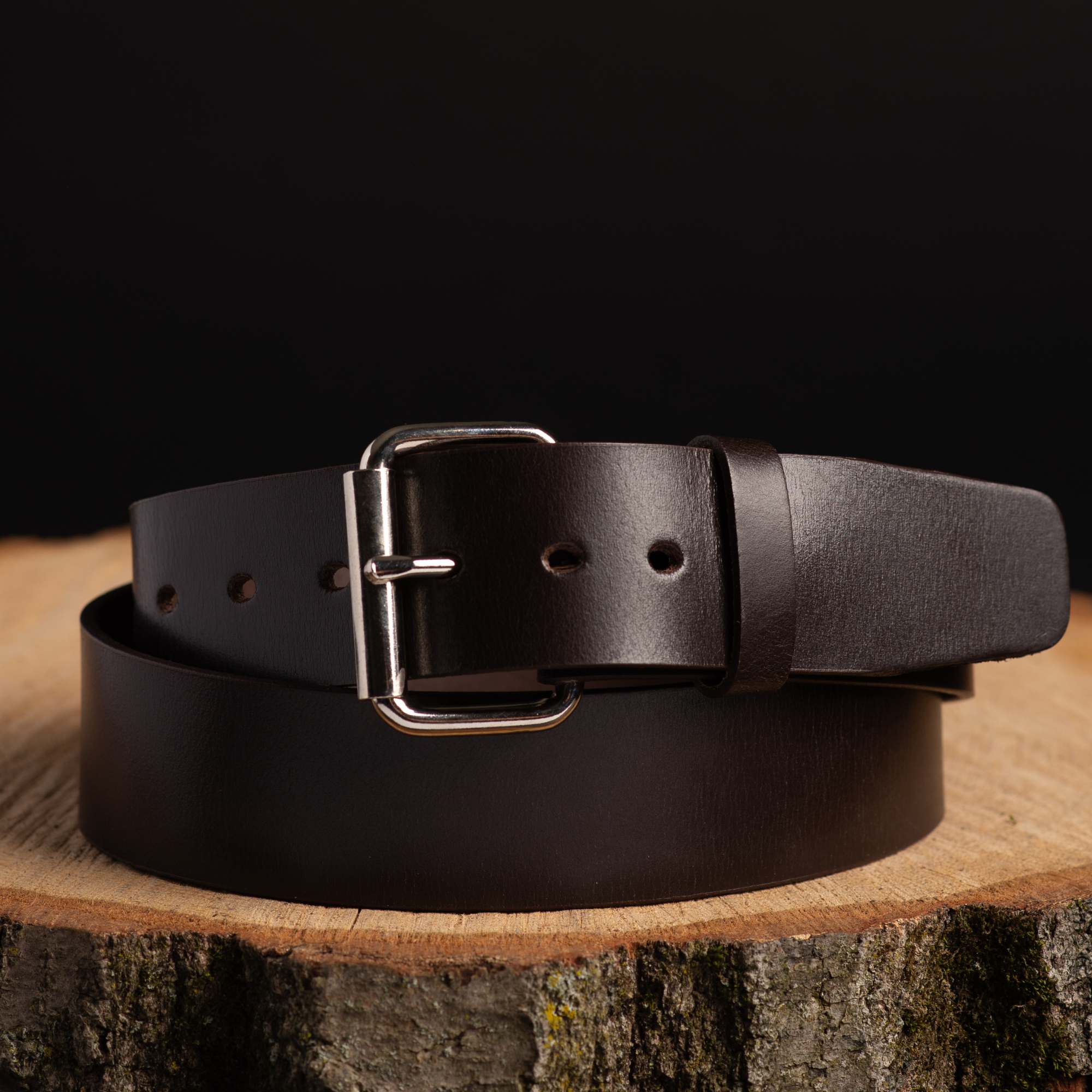Dark brown leather belt with silver buckle displayed on rustic wood, outdoor gear accessory