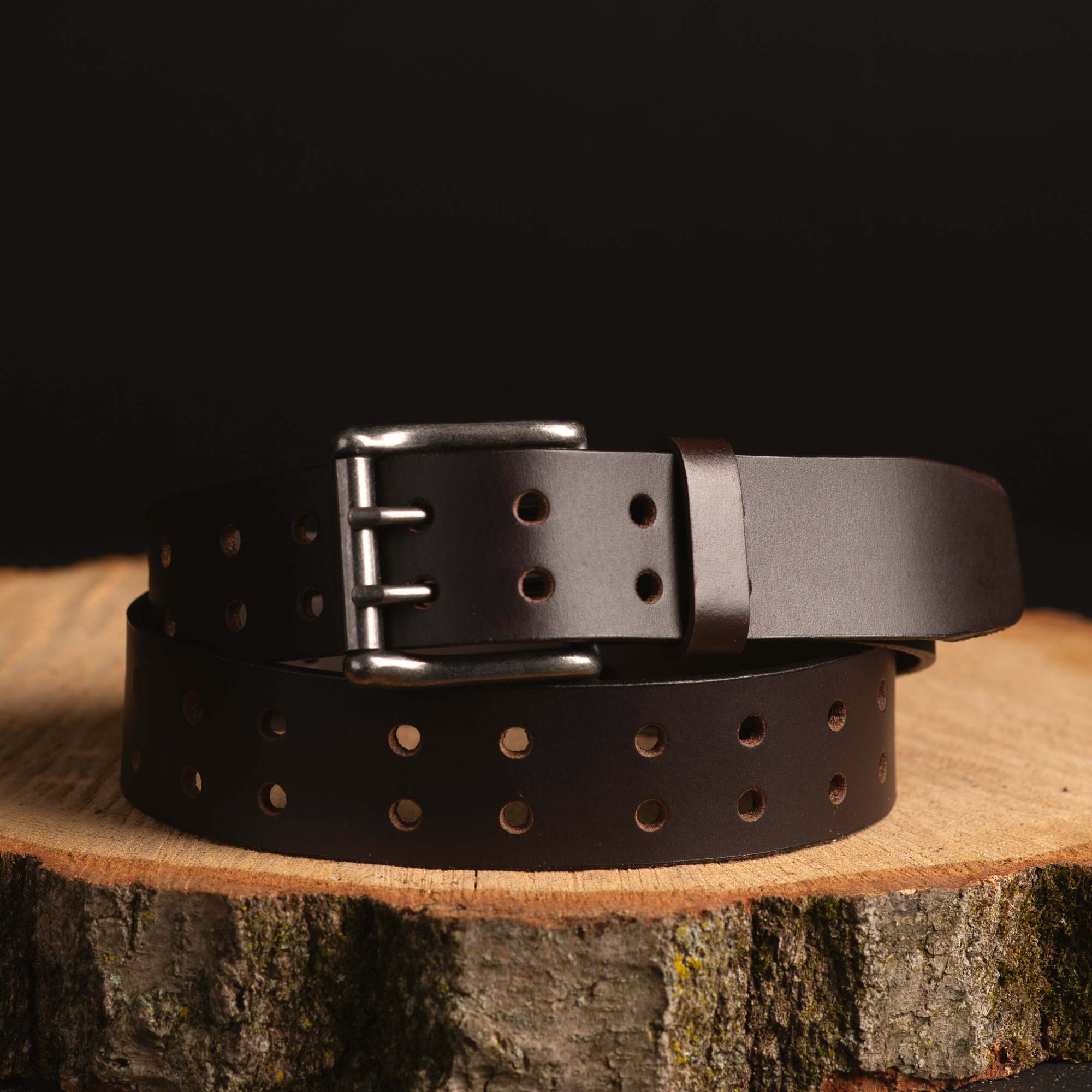 Double prong dark brown leather belt with multiple holes on wood, outdoor gear accessory