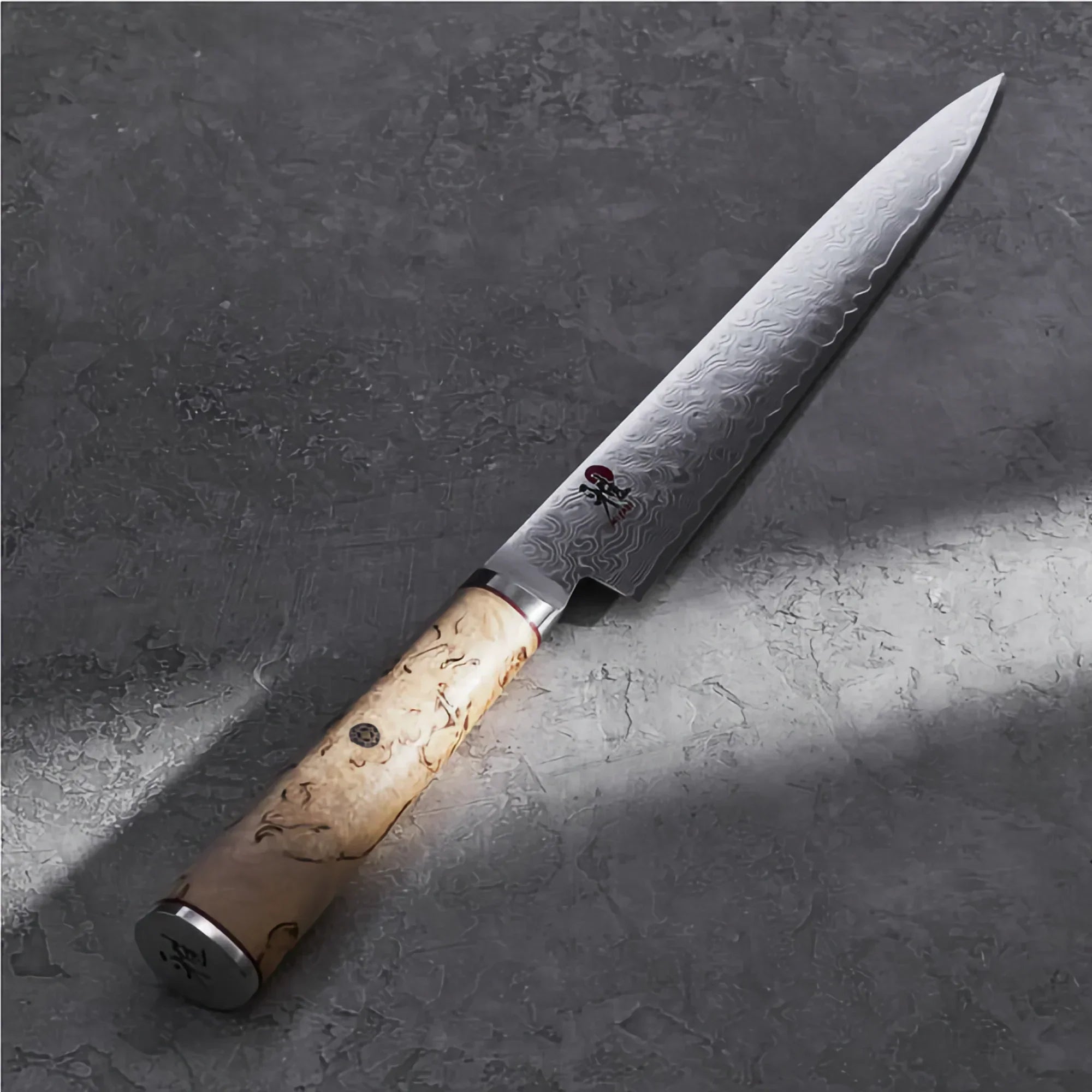 Damascus steel Sujihiki slicing knife with patterned blade and wood handle on stone surface
