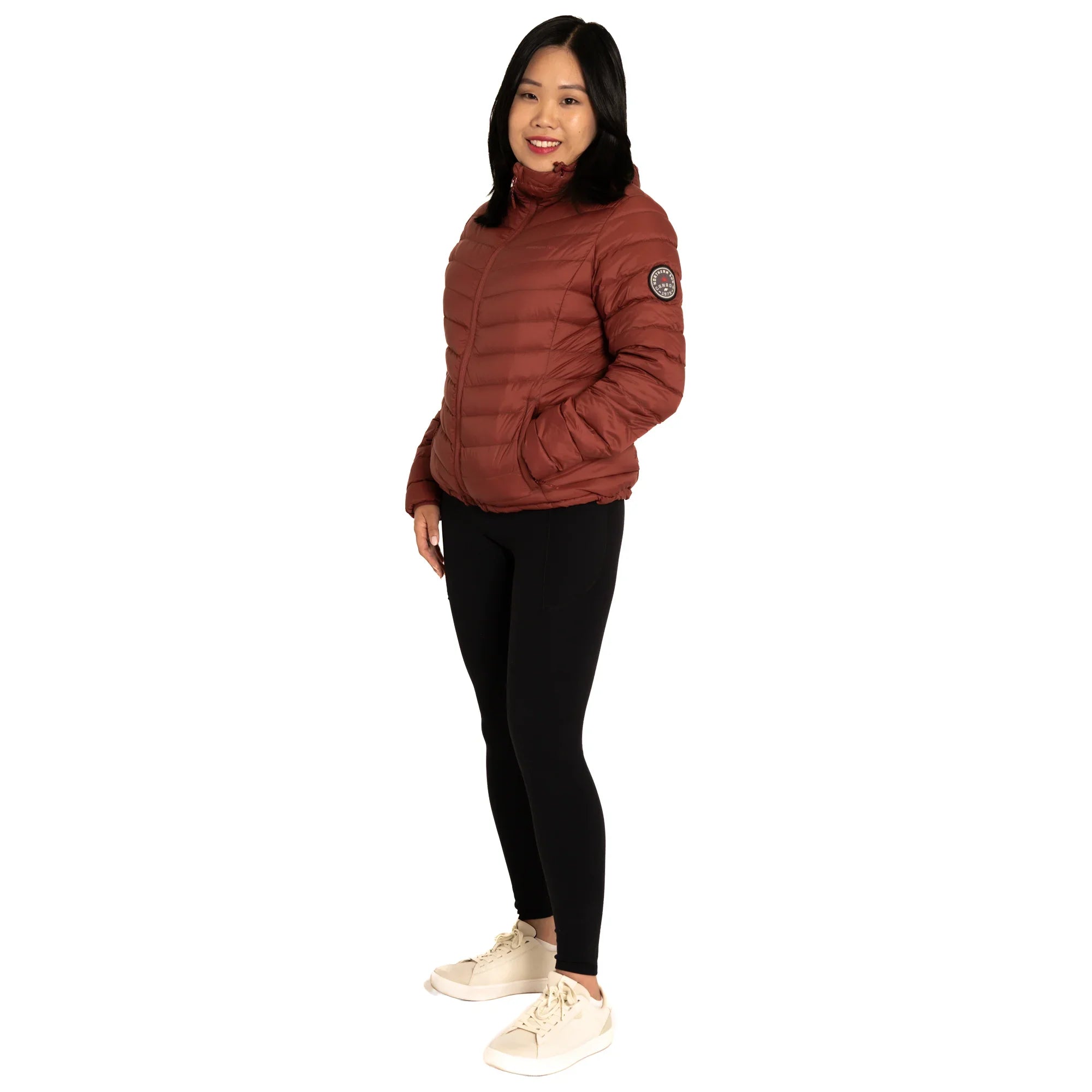 Woman in brown puffer jacket, black leggings, and white sneakers on white background