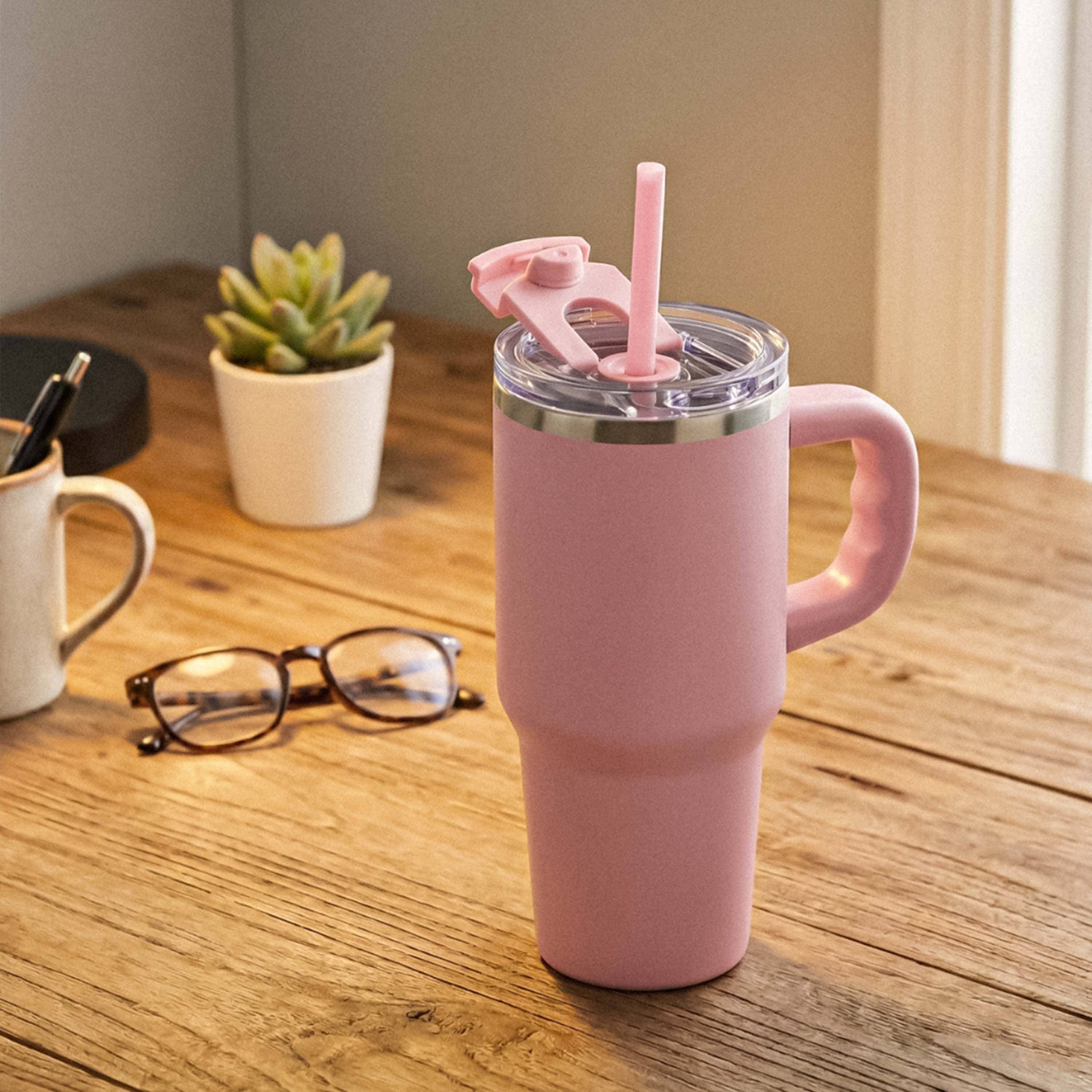 Pink insulated travel mug with handle, straw, and flip lid on a wooden desk indoors