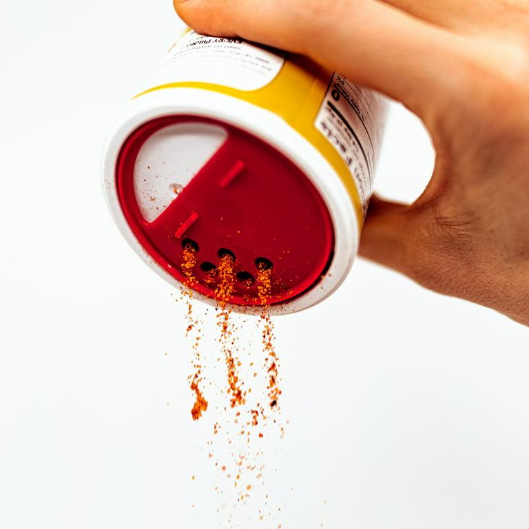 Hand pouring spice blend from shaker with red lid against white background