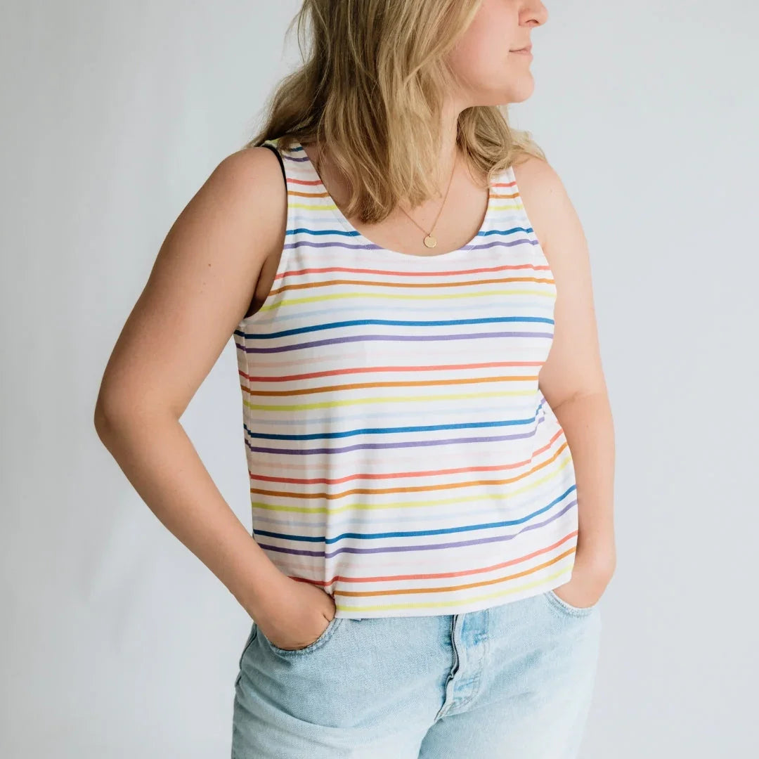 Woman in rainbow striped tank top and light denim jeans against white background