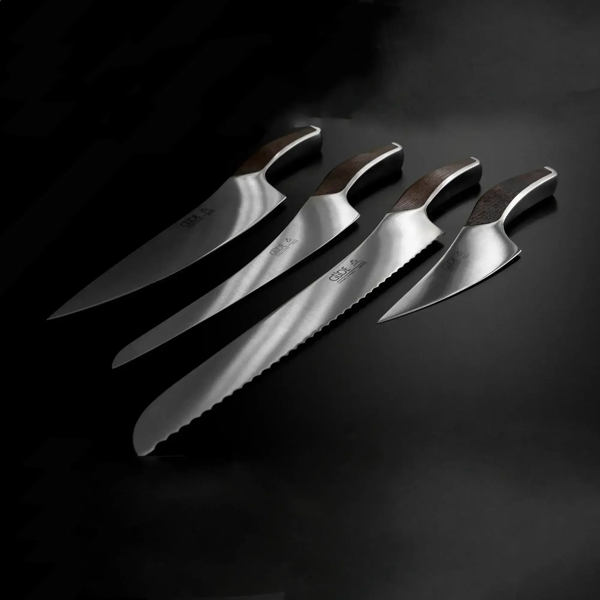 Set of four stainless steel kitchen knives with dark wood handles on a black background