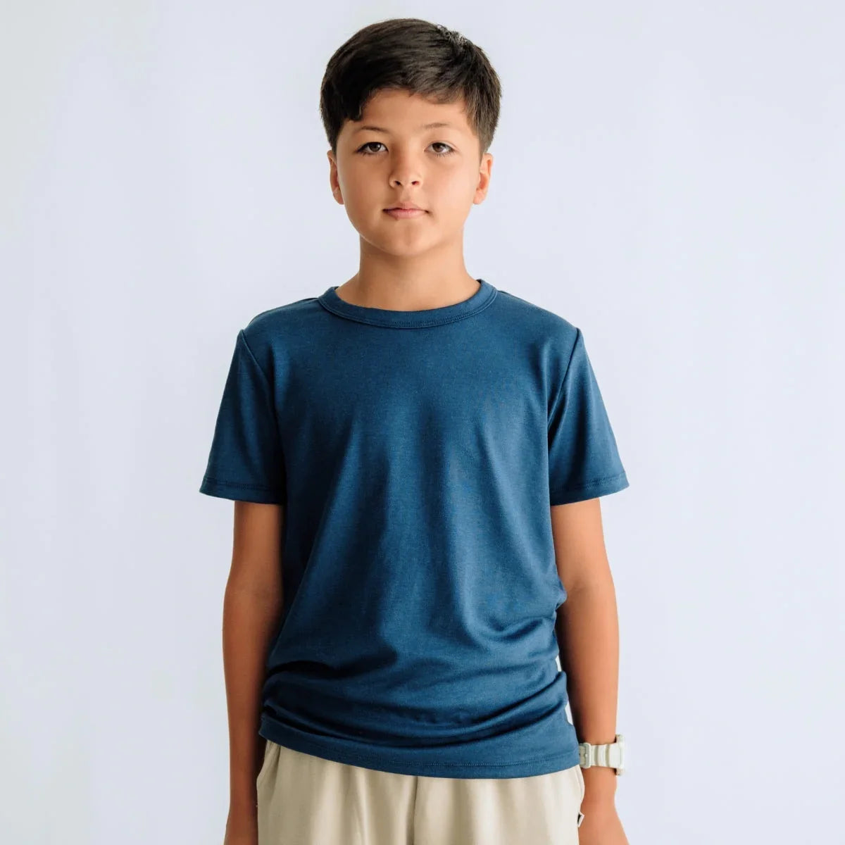 Boy in blue t-shirt and beige shorts standing against a plain white background