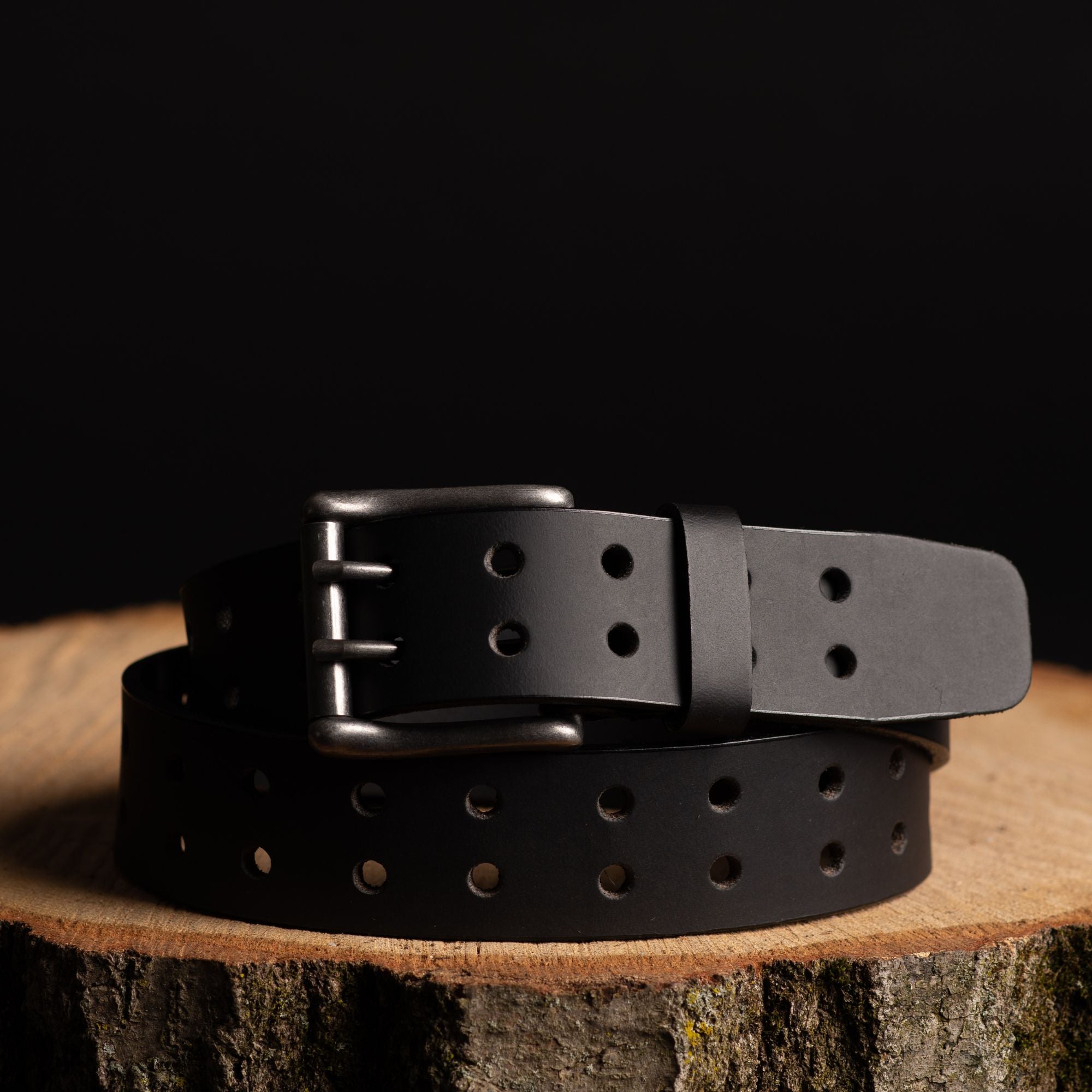 Black leather utility belt with double-prong buckle, displayed on wood, ideal for outdoor gear.
