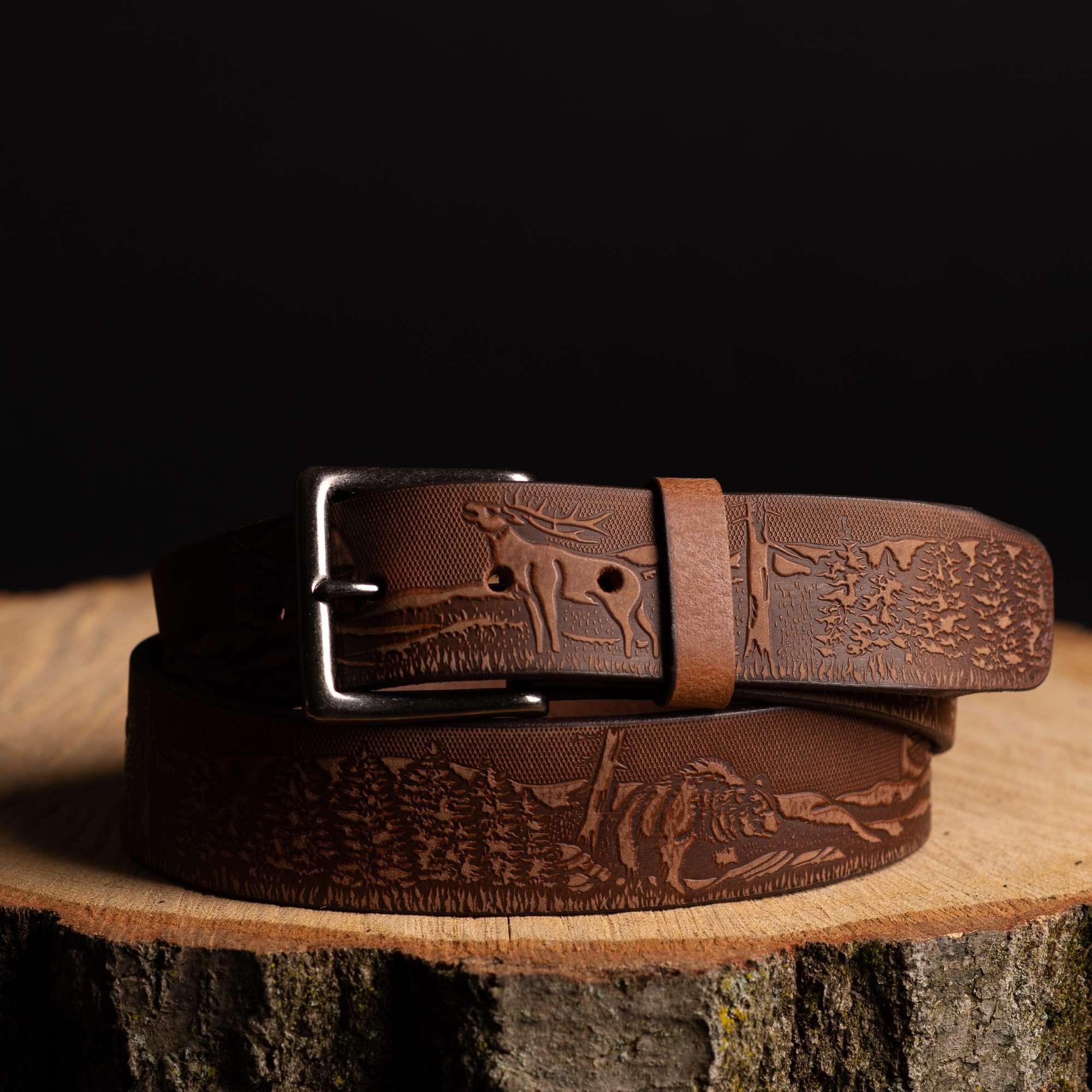Brown leather belt with forest and deer embossed design on wood, camping and hunting gear