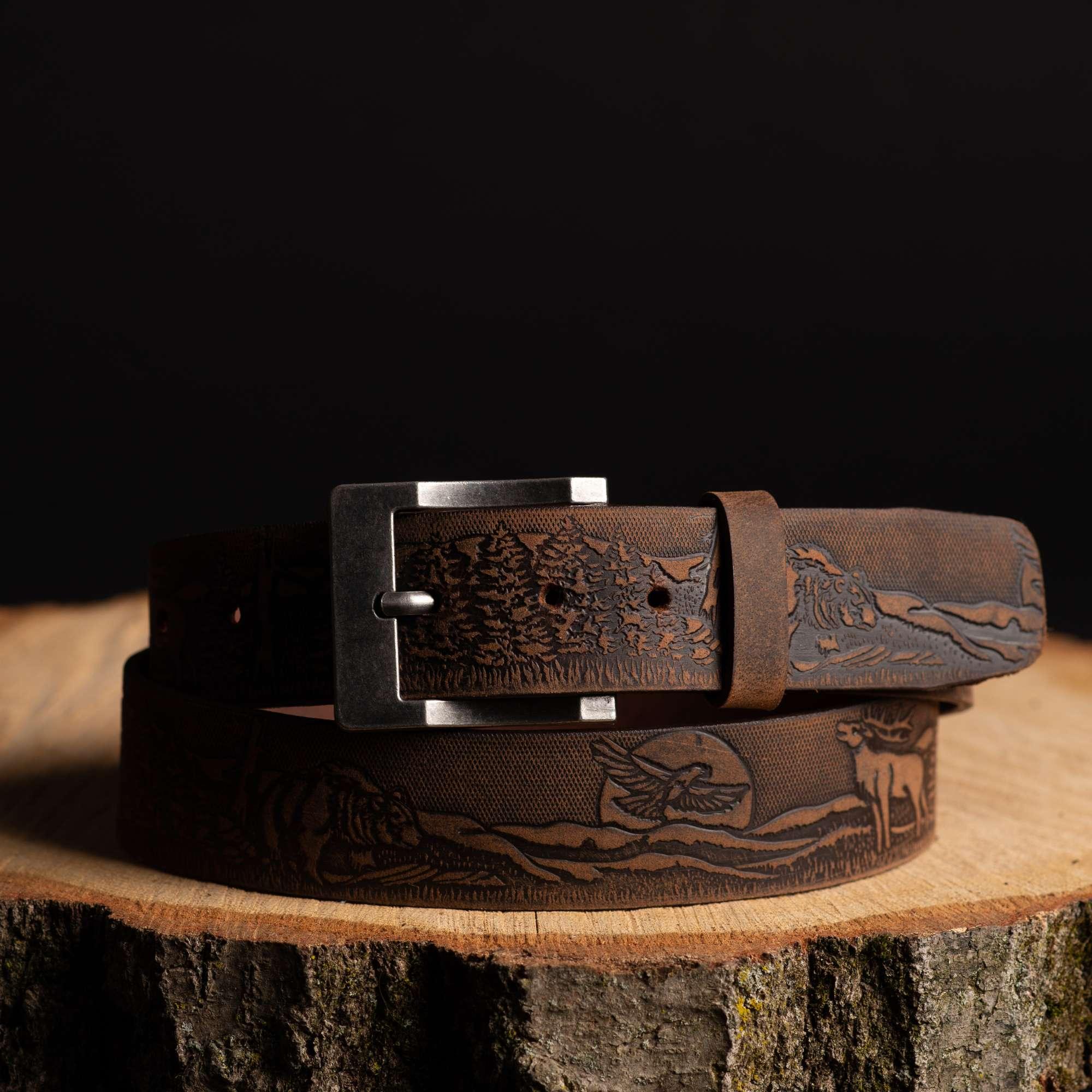 Brown leather belt with engraved wildlife and nature scene, outdoor accessory on wood