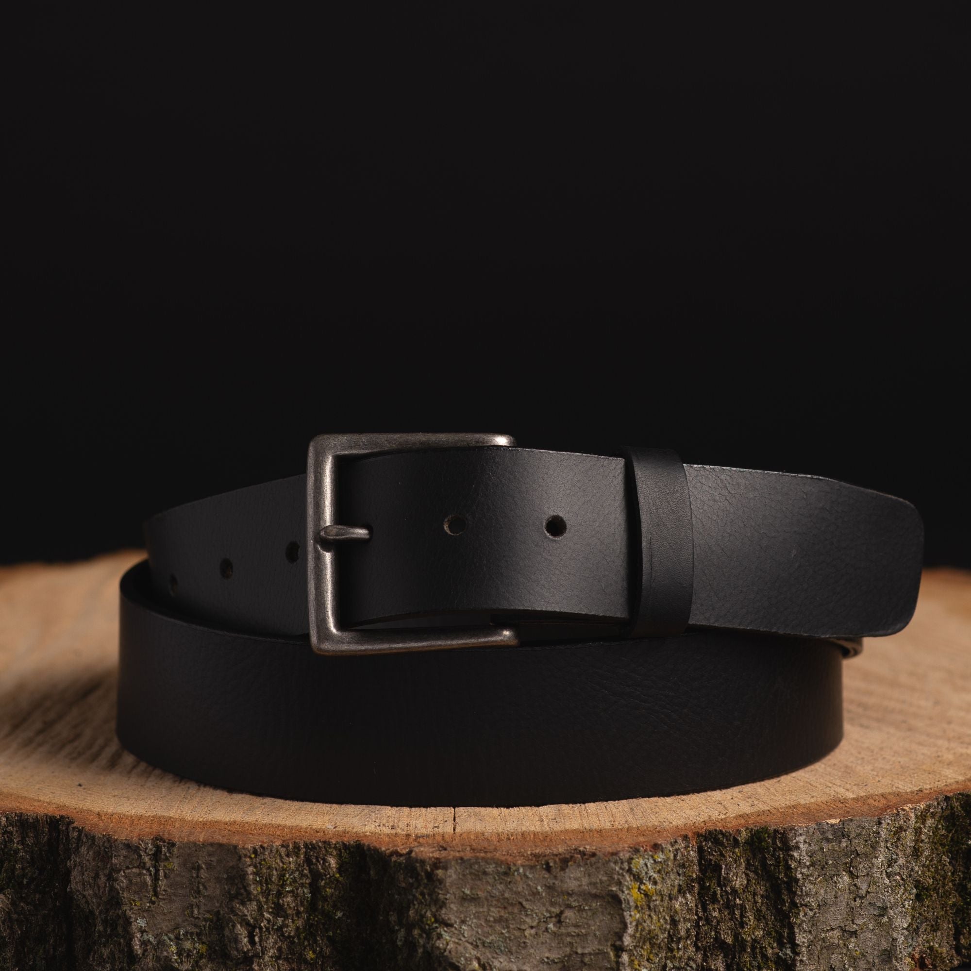 Black leather belt with metal buckle on wood slab, outdoor gear accessory