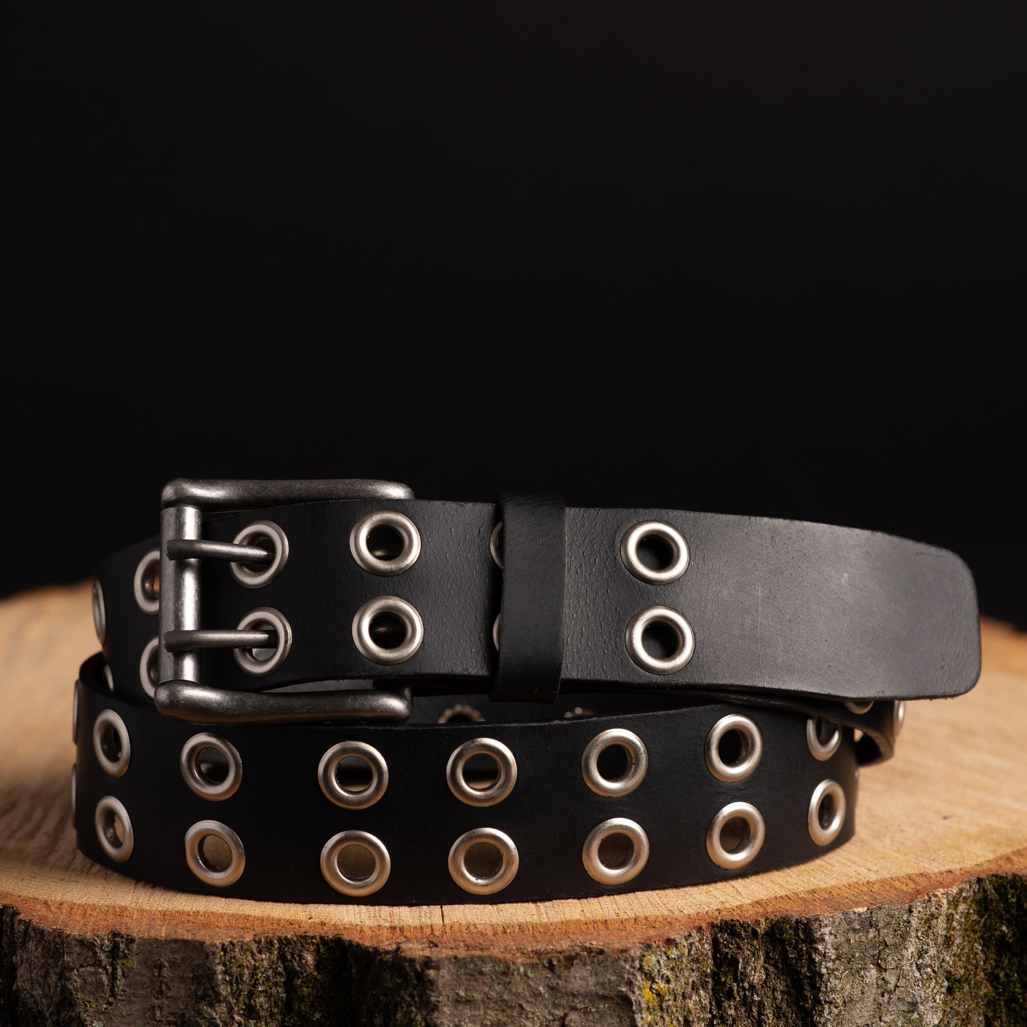 Black double grommet leather belt with silver eyelets on wooden surface, outdoor gear